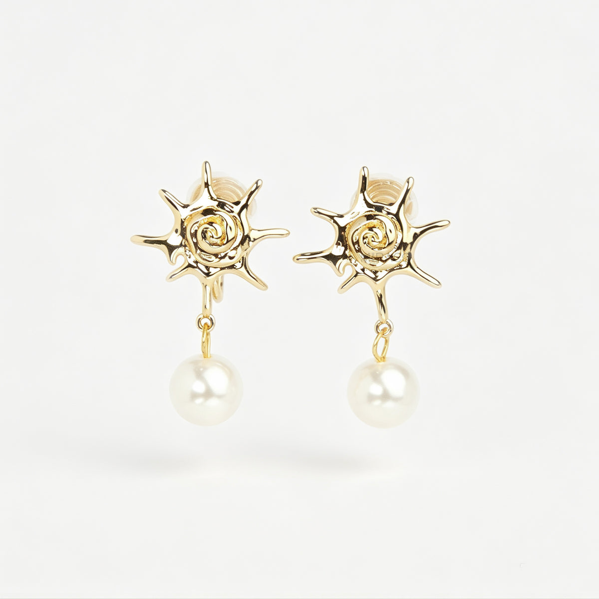 Gold coil-back clip-on earrings with a swirled sunburst star motif and a dangling white pearl 