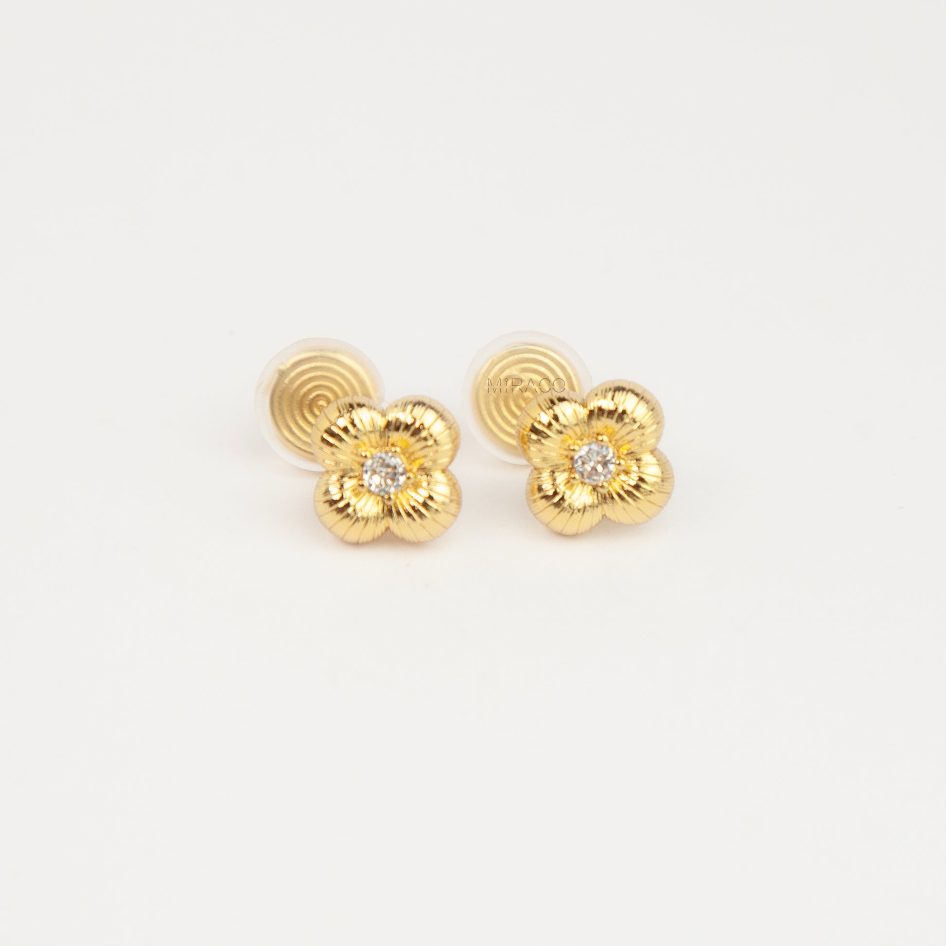 Textured gold clover-shaped floral clip-on stud earrings set with a round central crystal and a coil-back closure.