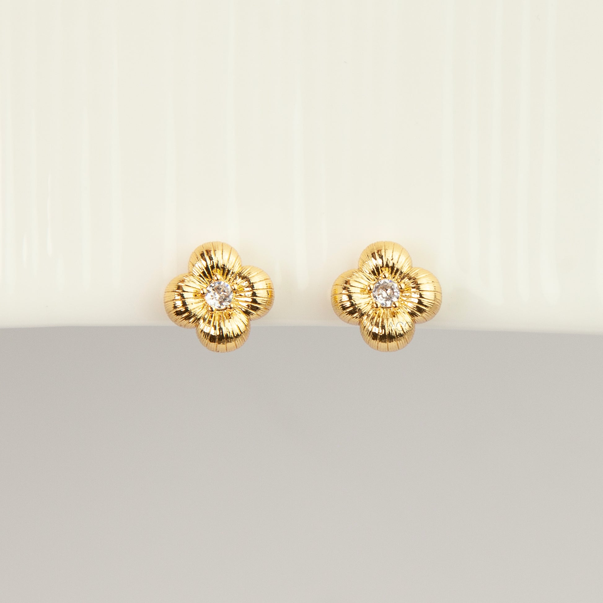 Textured gold clover-shaped floral clip-on stud earrings set with a round central crystal and a coil-back closure.