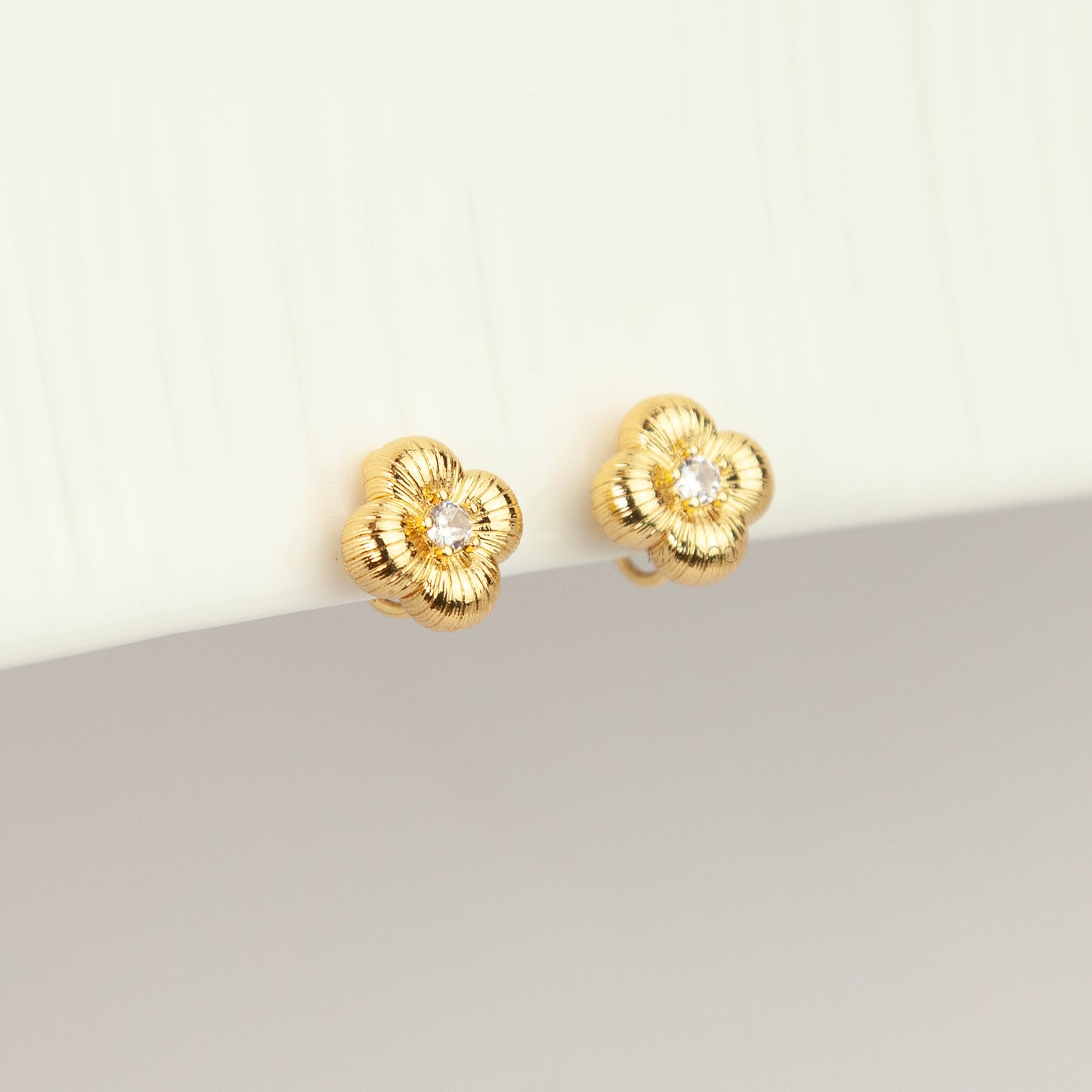 Textured gold clover-shaped floral clip-on stud earrings set with a round central crystal and a coil-back closure.