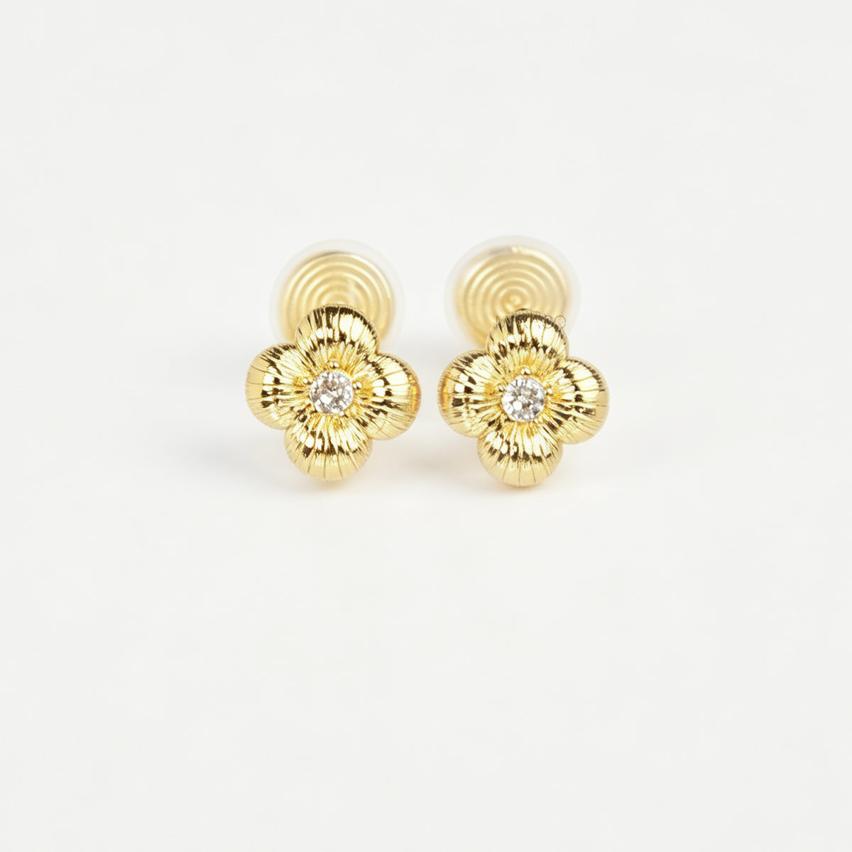 Textured gold clover-shaped floral clip-on stud earrings set with a round central crystal and a coil-back closure.