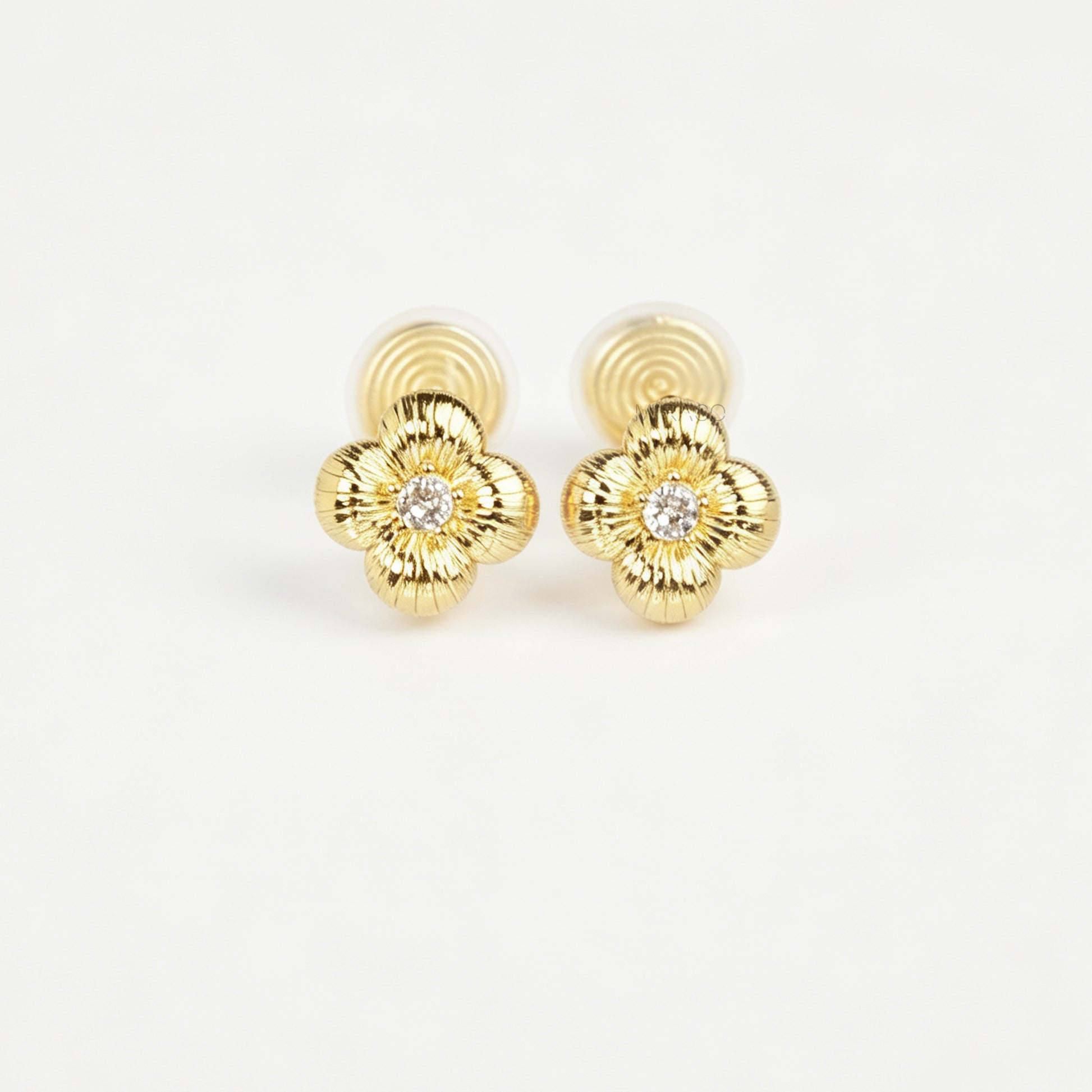 Textured gold clover-shaped floral clip-on stud earrings set with a round central crystal and a coil-back closure.