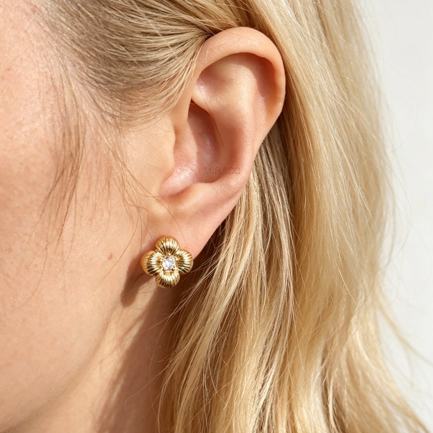 Textured gold clover-shaped floral clip-on stud earrings set with a round central crystal and a coil-back closure.