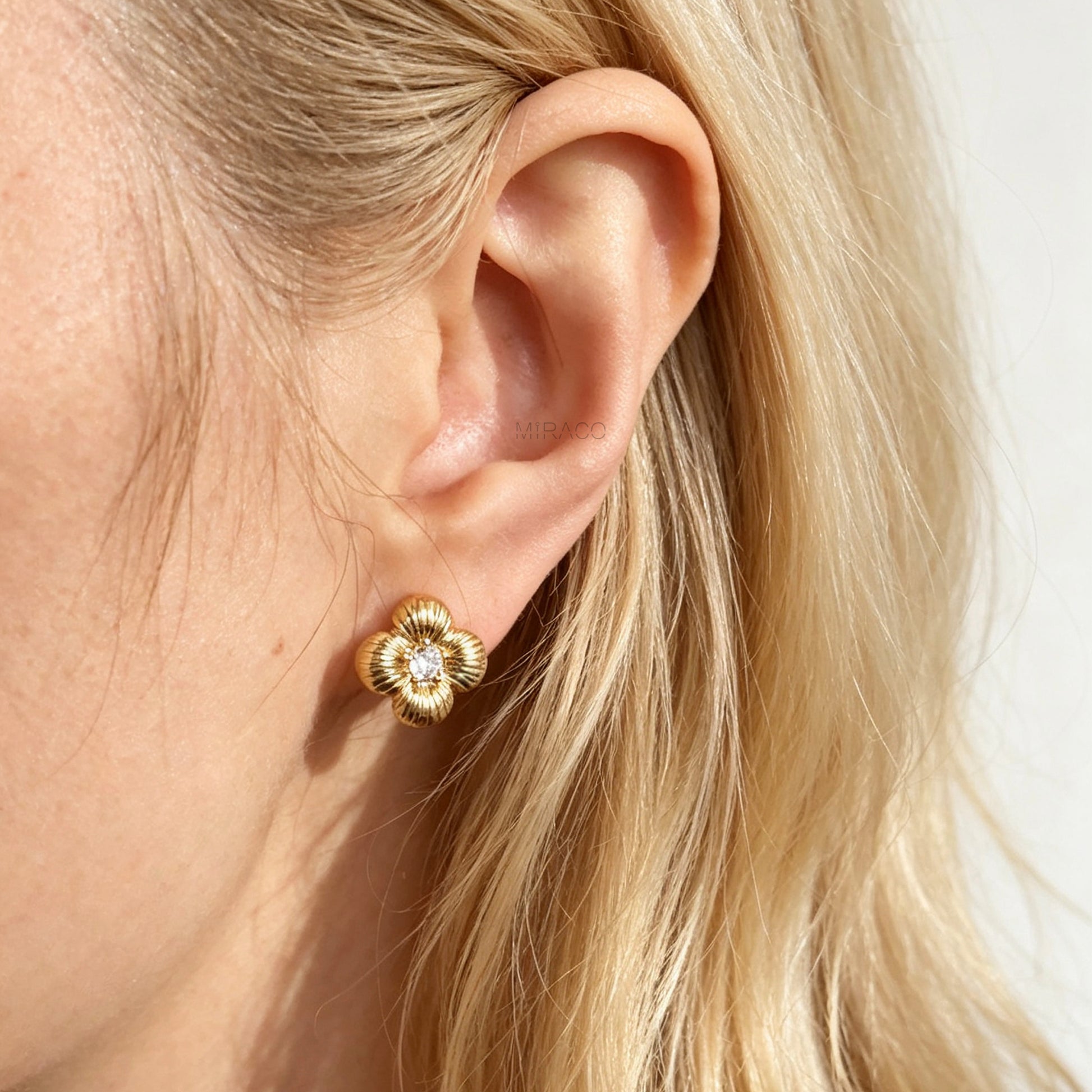 Textured gold clover-shaped floral clip-on stud earrings set with a round central crystal and a coil-back closure.