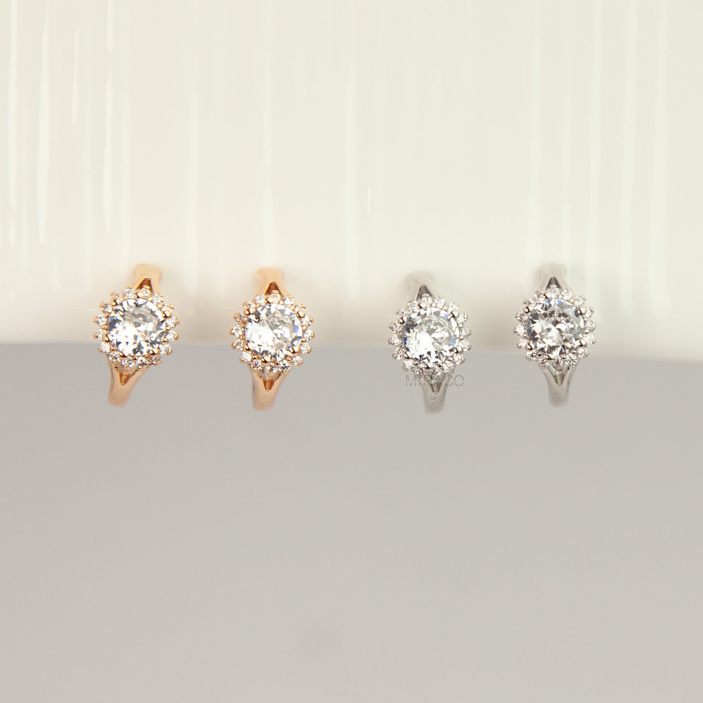 Gold and silver halo crystal coil-back clip-on huggie earrings set with a round solitaire gem surrounded by pave stones.