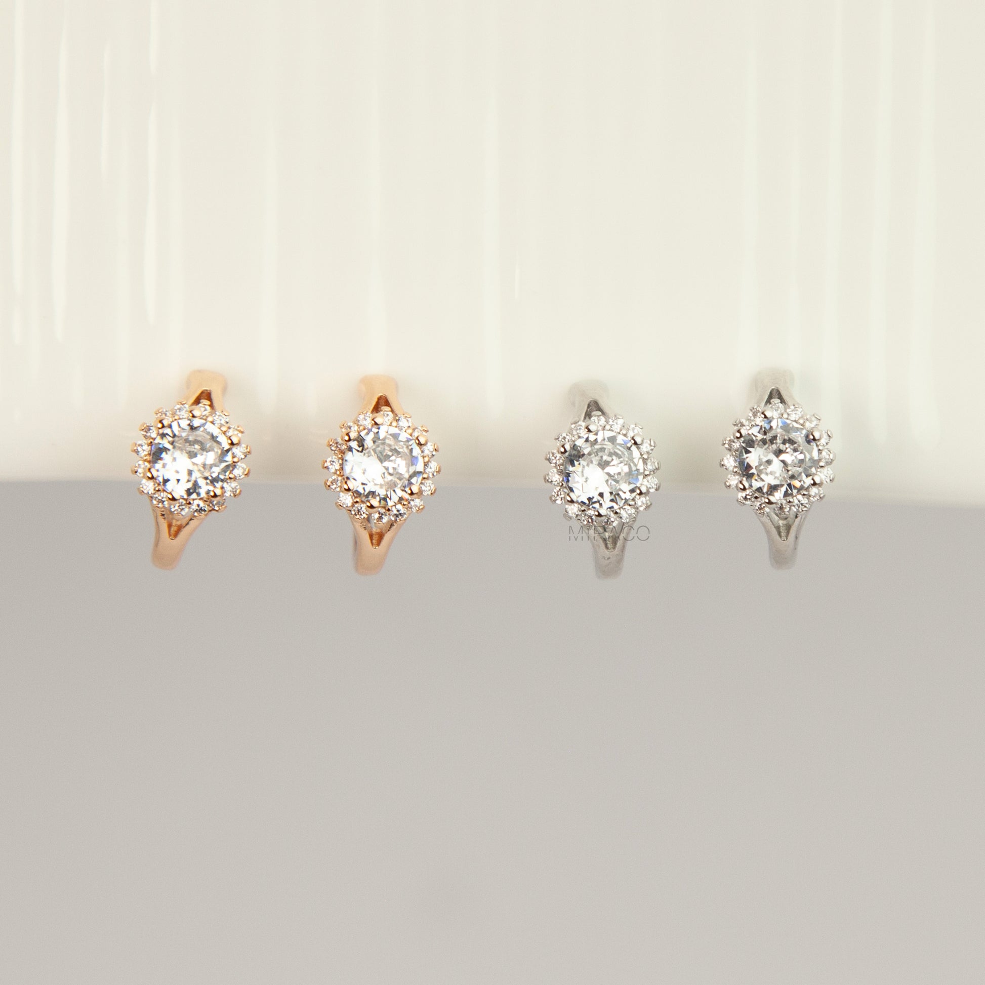 Gold and silver halo crystal coil-back clip-on huggie earrings set with a round solitaire gem surrounded by pave stones.