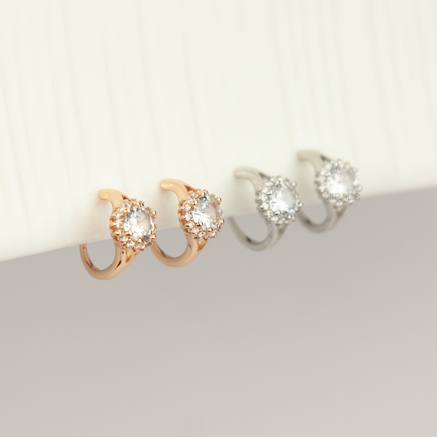 Gold and silver halo crystal coil-back clip-on huggie earrings set with a round solitaire gem surrounded by pave stones.