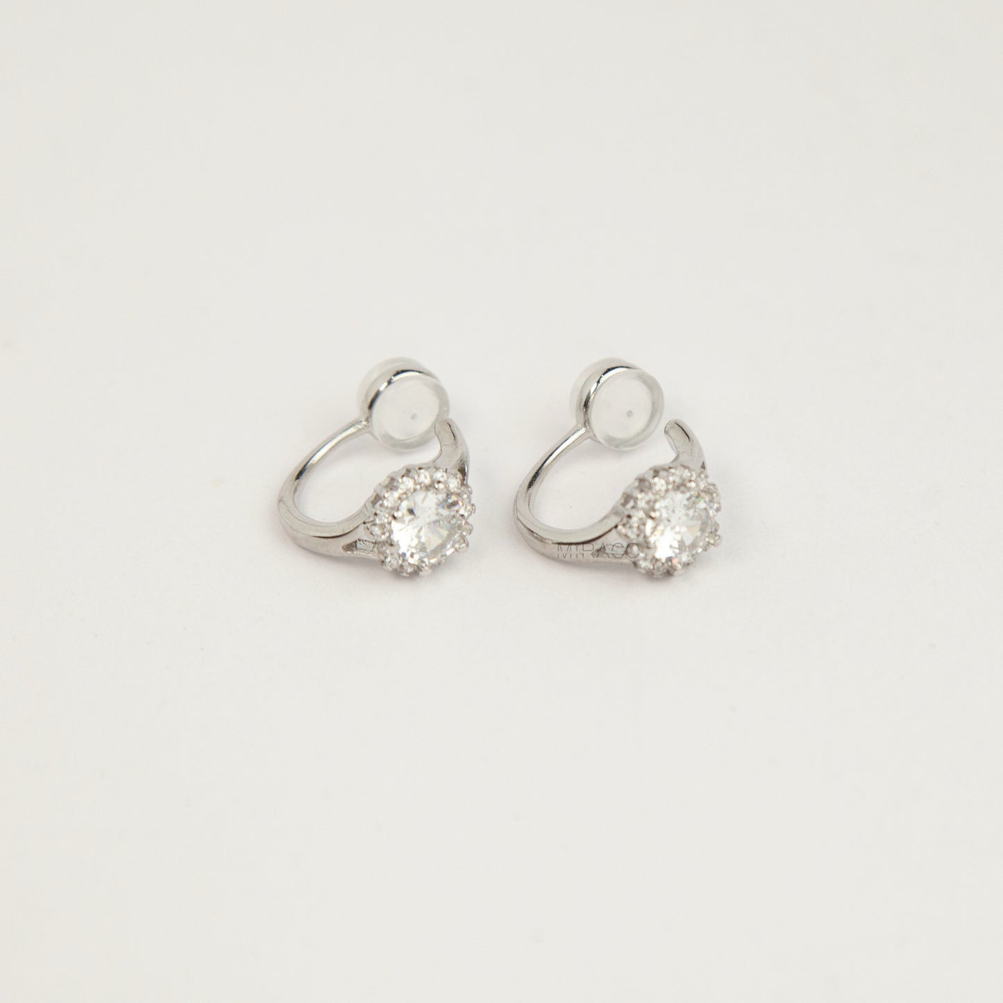 silver halo crystal coil-back clip-on huggie earrings set with a round solitaire gem surrounded by pave stones.