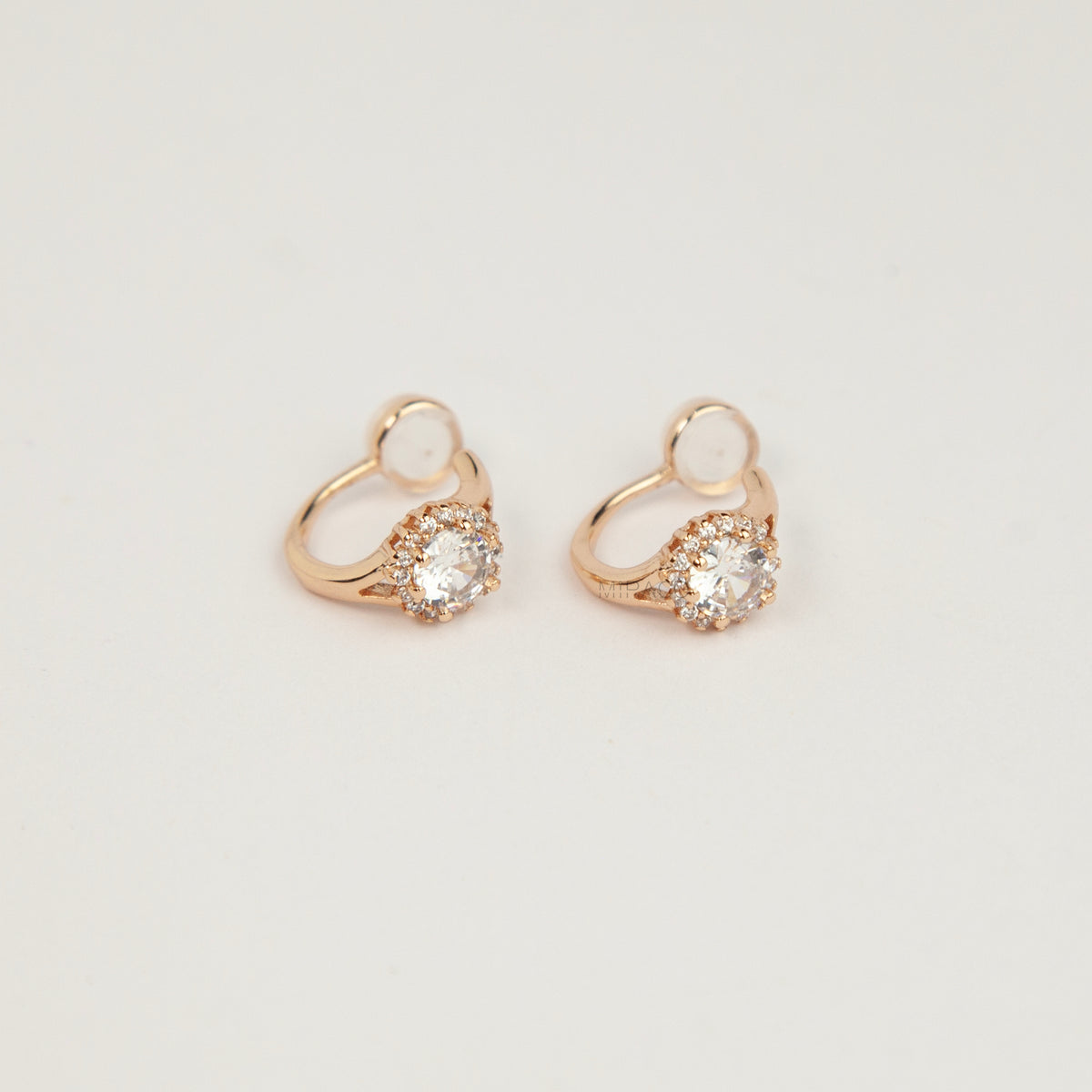Gold halo crystal coil-back clip-on huggie earrings set with a round solitaire gem surrounded by pave stones.