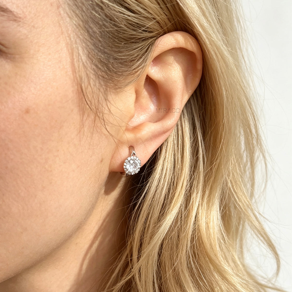 Gold and silver halo crystal coil-back clip-on huggie earrings set with a round solitaire gem surrounded by pave stones.