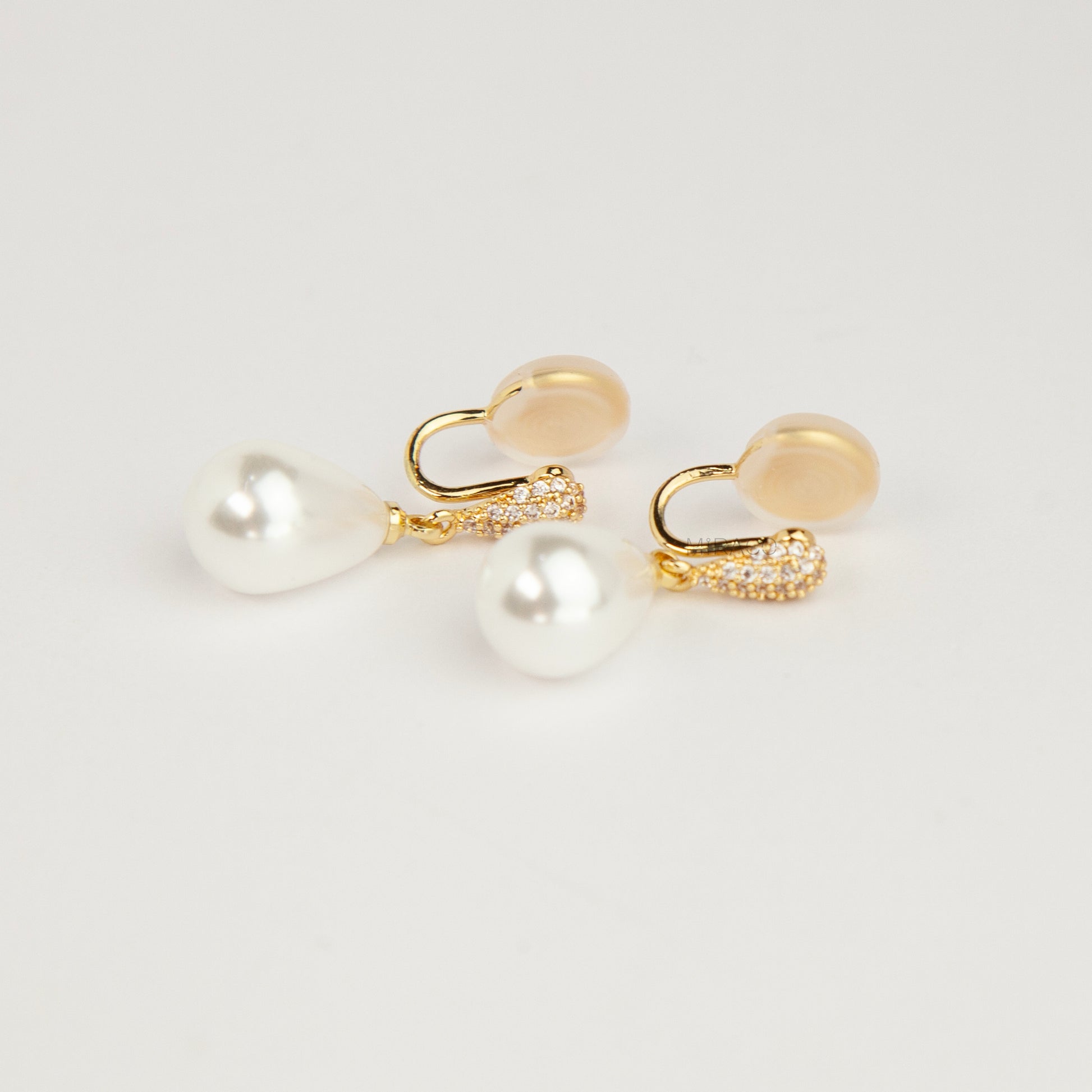 Gold coil-back clip-on drop earrings featuring a pave crystal teardrop stud and dangling white pear-shaped pearl 