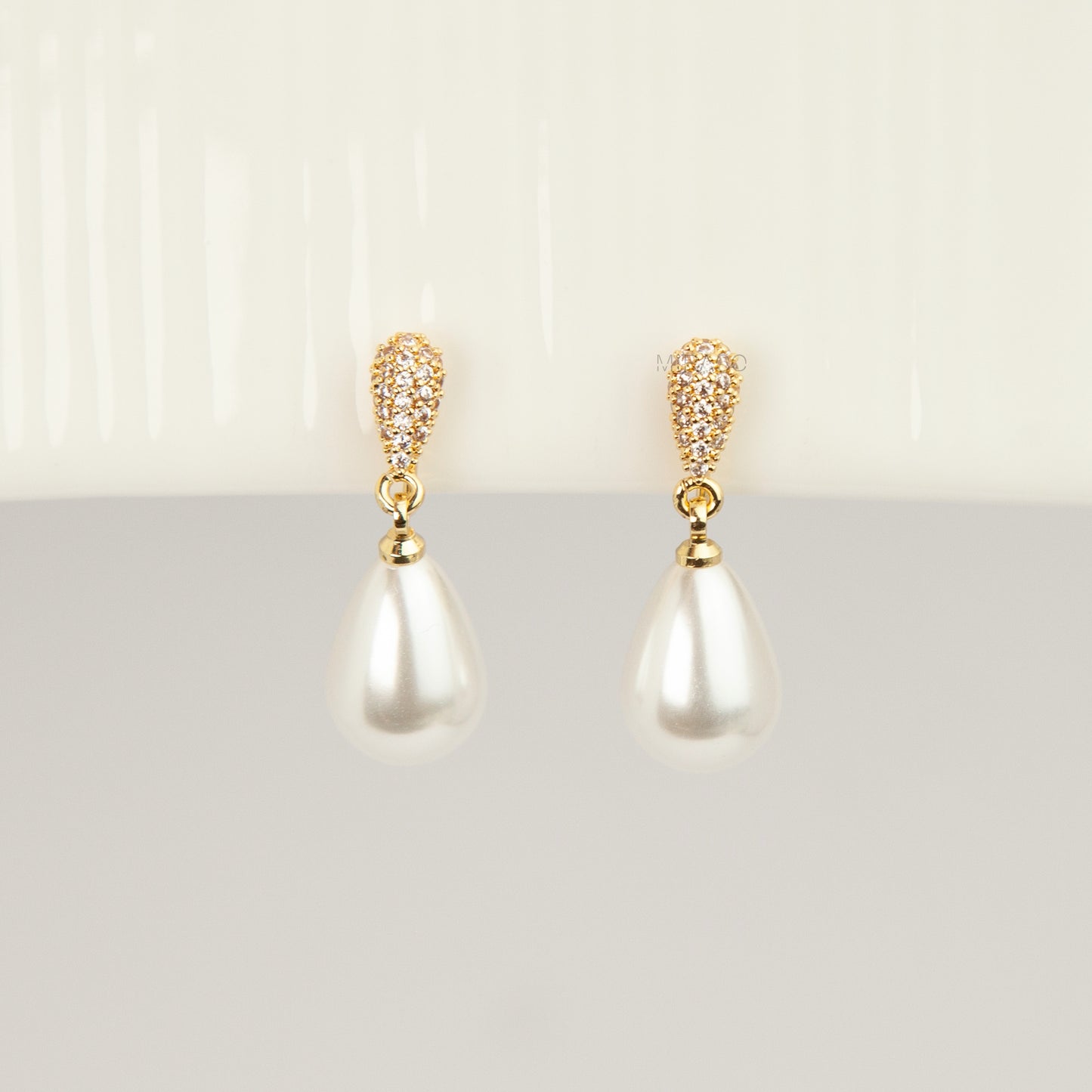 Gold coil-back clip-on drop earrings featuring a pave crystal teardrop stud and dangling white pear-shaped pearl 