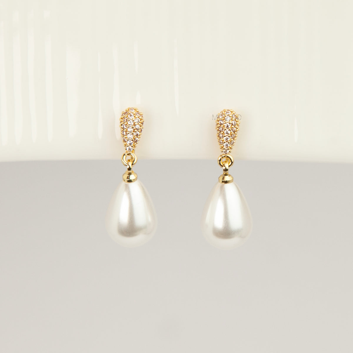 Gold coil-back clip-on drop earrings featuring a pave crystal teardrop stud and dangling white pear-shaped pearl 