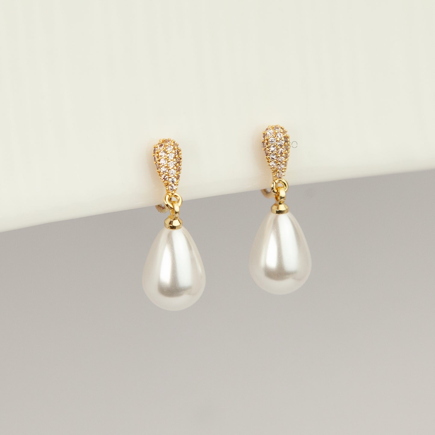 Gold coil-back clip-on drop earrings featuring a pave crystal teardrop stud and dangling white pear-shaped pearl 