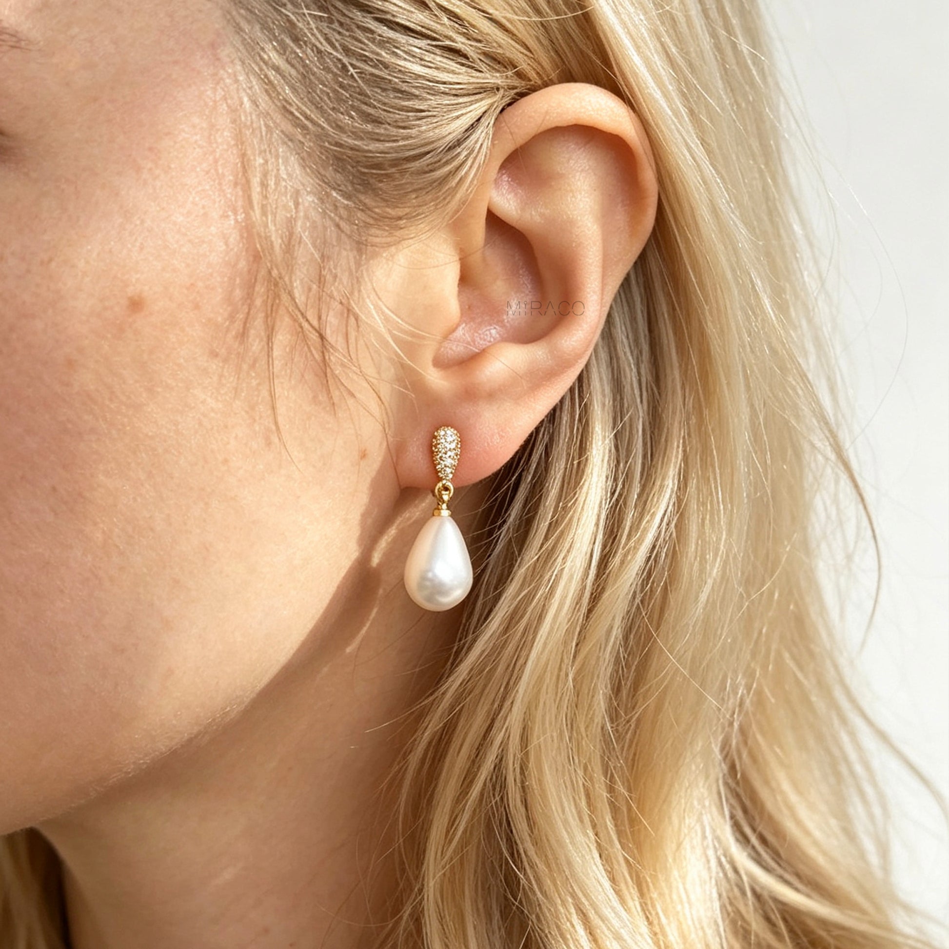 Gold coil-back clip-on drop earrings featuring a pave crystal teardrop stud and dangling white pear-shaped pearl 