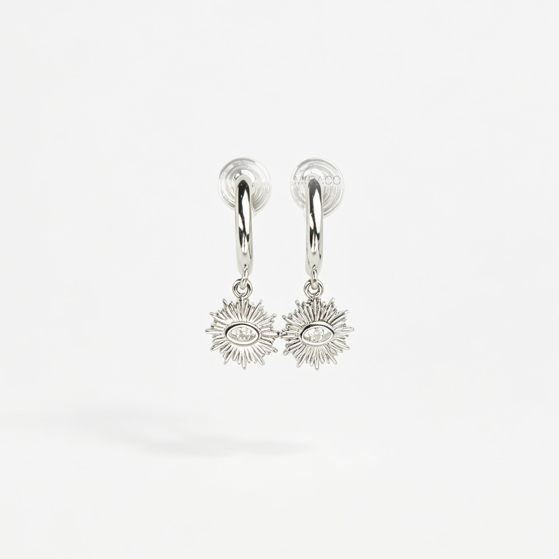 Silver coil-back clip-on hoop earrings featuring a dangling sunburst charm with a central oval crystal evil eye motif 