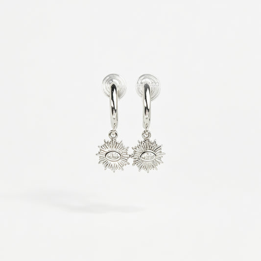 Silver coil-back clip-on hoop earrings featuring a dangling sunburst charm with a central oval crystal evil eye motif 