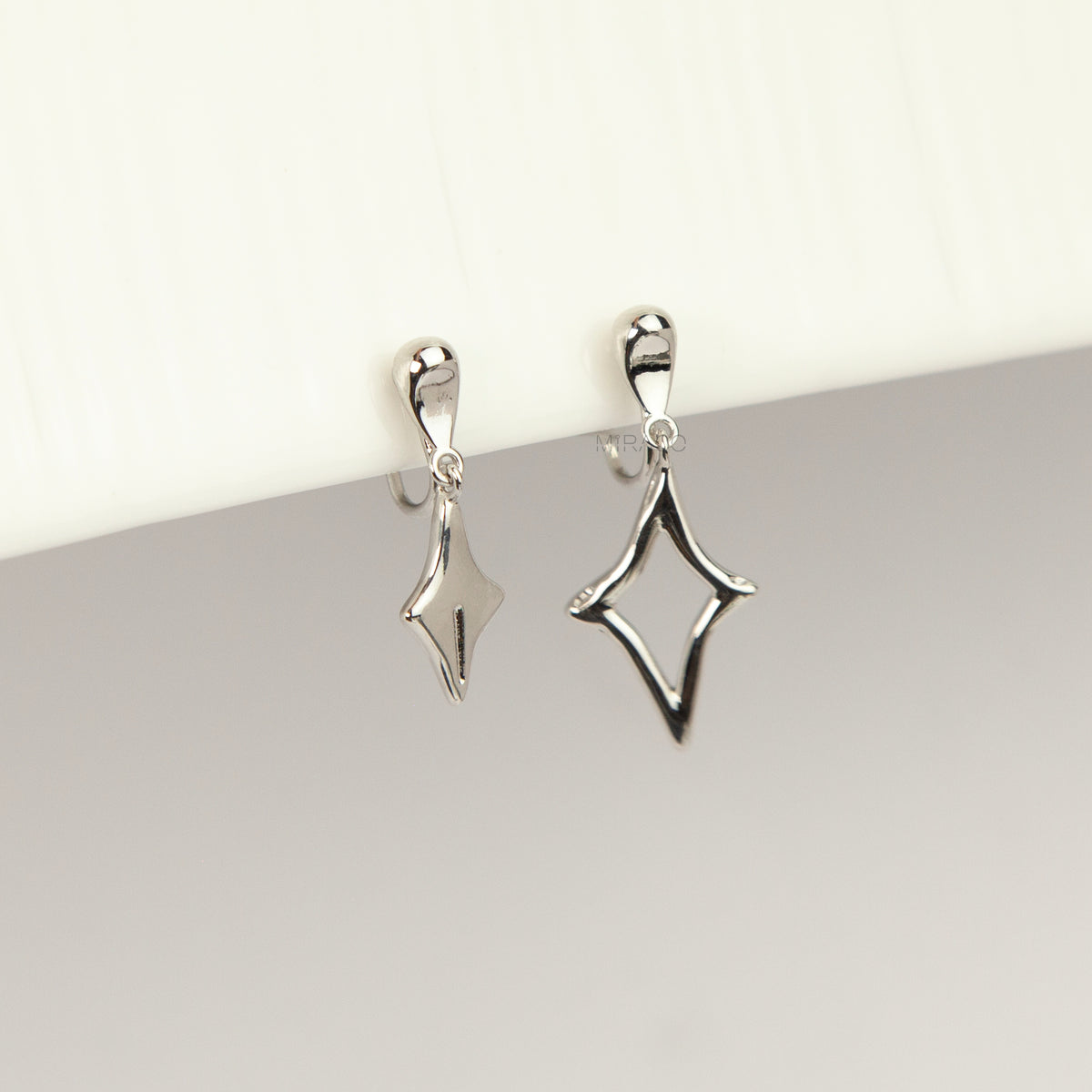 Silver coil-back clip-on drop earrings featuring mismatched solid and hollow four-point starburst charms