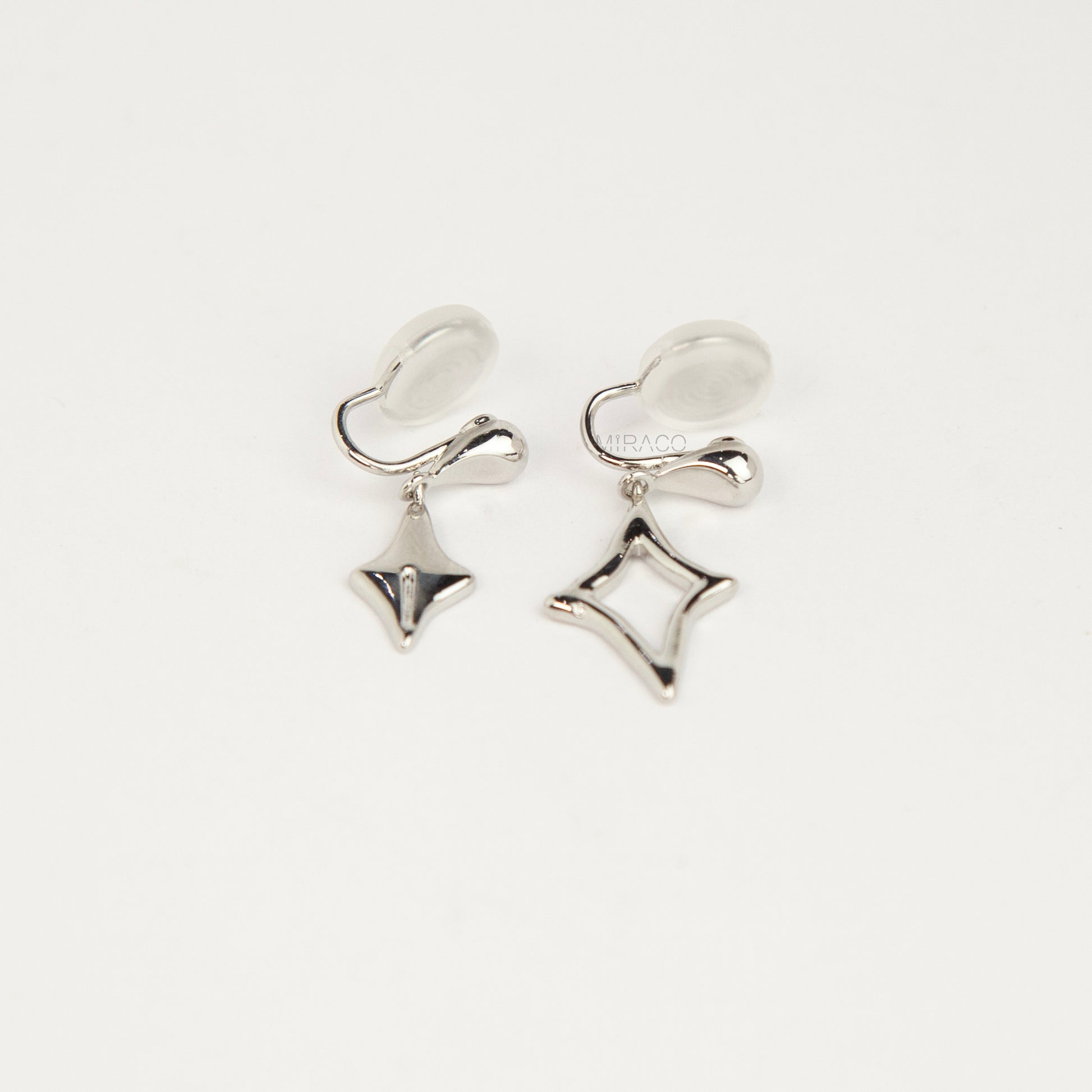 Silver coil-back clip-on drop earrings featuring mismatched solid and hollow four-point starburst charms