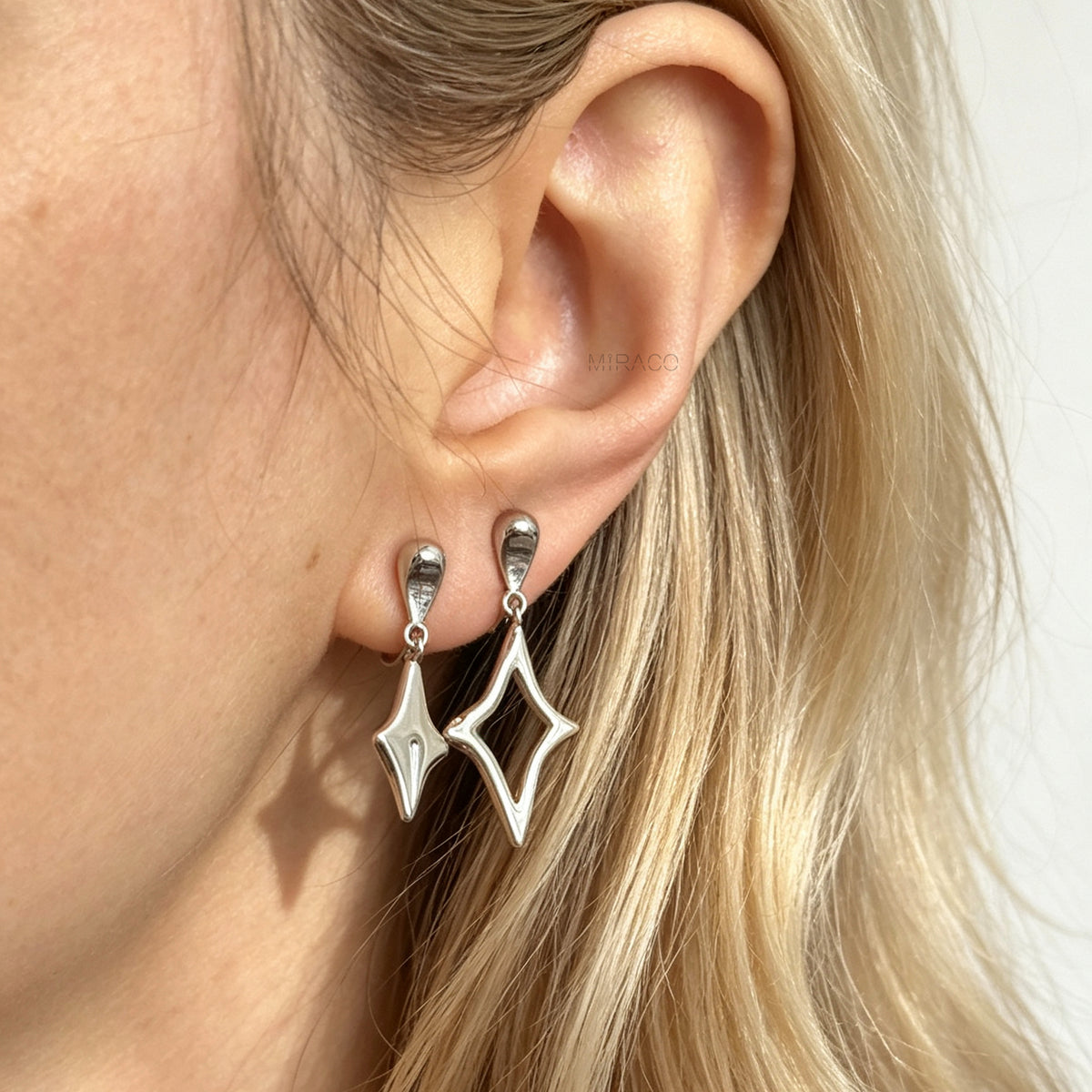 Silver coil-back clip-on drop earrings featuring mismatched solid and hollow four-point starburst charms, styled side by side on a single earlobe.