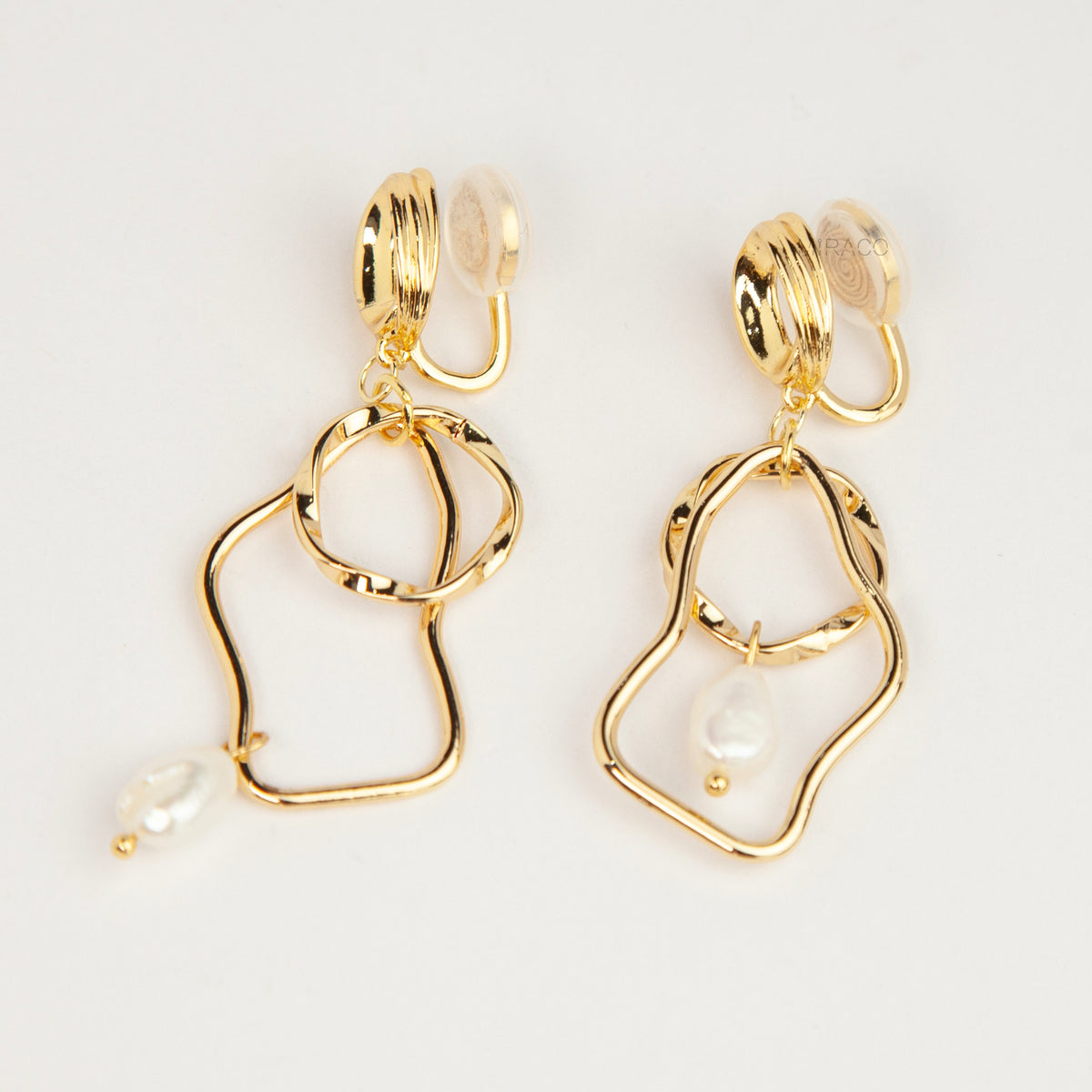 Gold coil-back clip-on statement earrings featuring abstract wavy geometric hoops and dangling teardrop pearl accents.