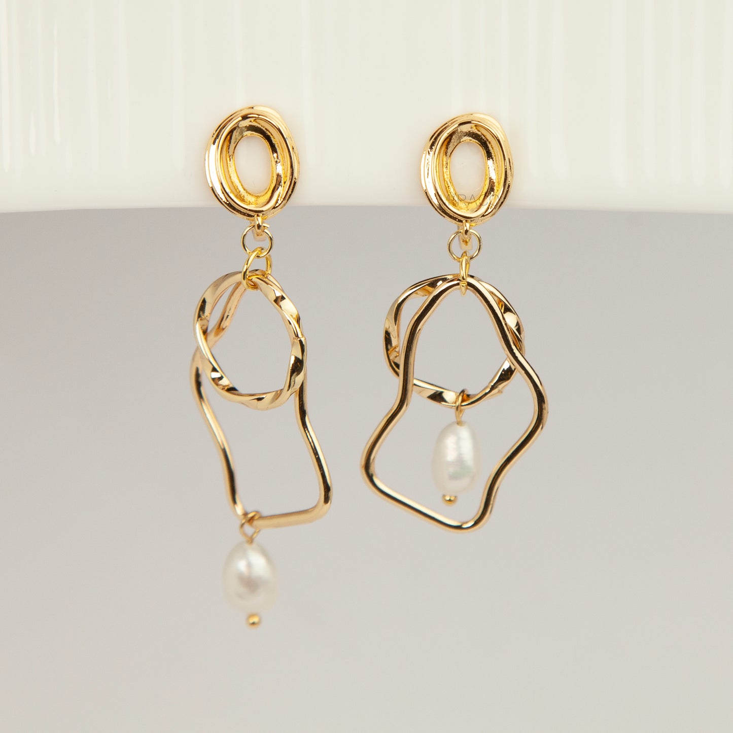 Gold coil-back clip-on statement earrings featuring abstract wavy geometric hoops and dangling teardrop pearl accents.