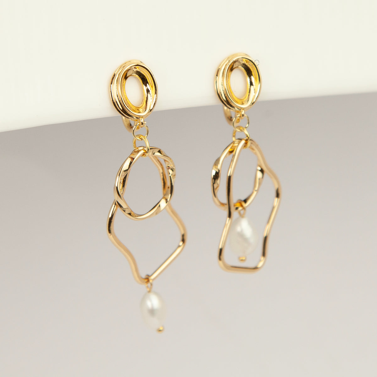 Gold coil-back clip-on statement earrings featuring abstract wavy geometric hoops and dangling teardrop pearl accents.