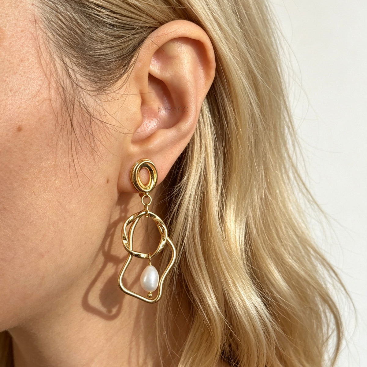 Gold coil-back clip-on statement earrings featuring abstract wavy geometric hoops and dangling teardrop pearl accents.