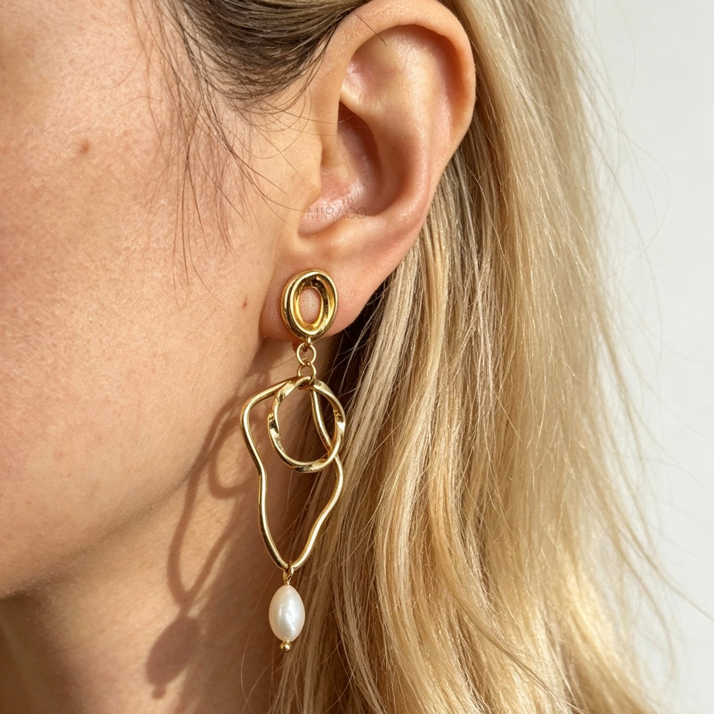 Gold coil-back clip-on statement earrings featuring abstract wavy geometric hoops and dangling teardrop pearl accents.