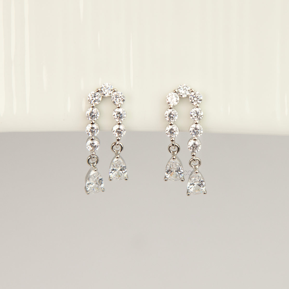 Silver non-pierced clip-on arch earrings with round silicone backs, paved with round cubic zirconia and finished with dangling teardrop crystal gems