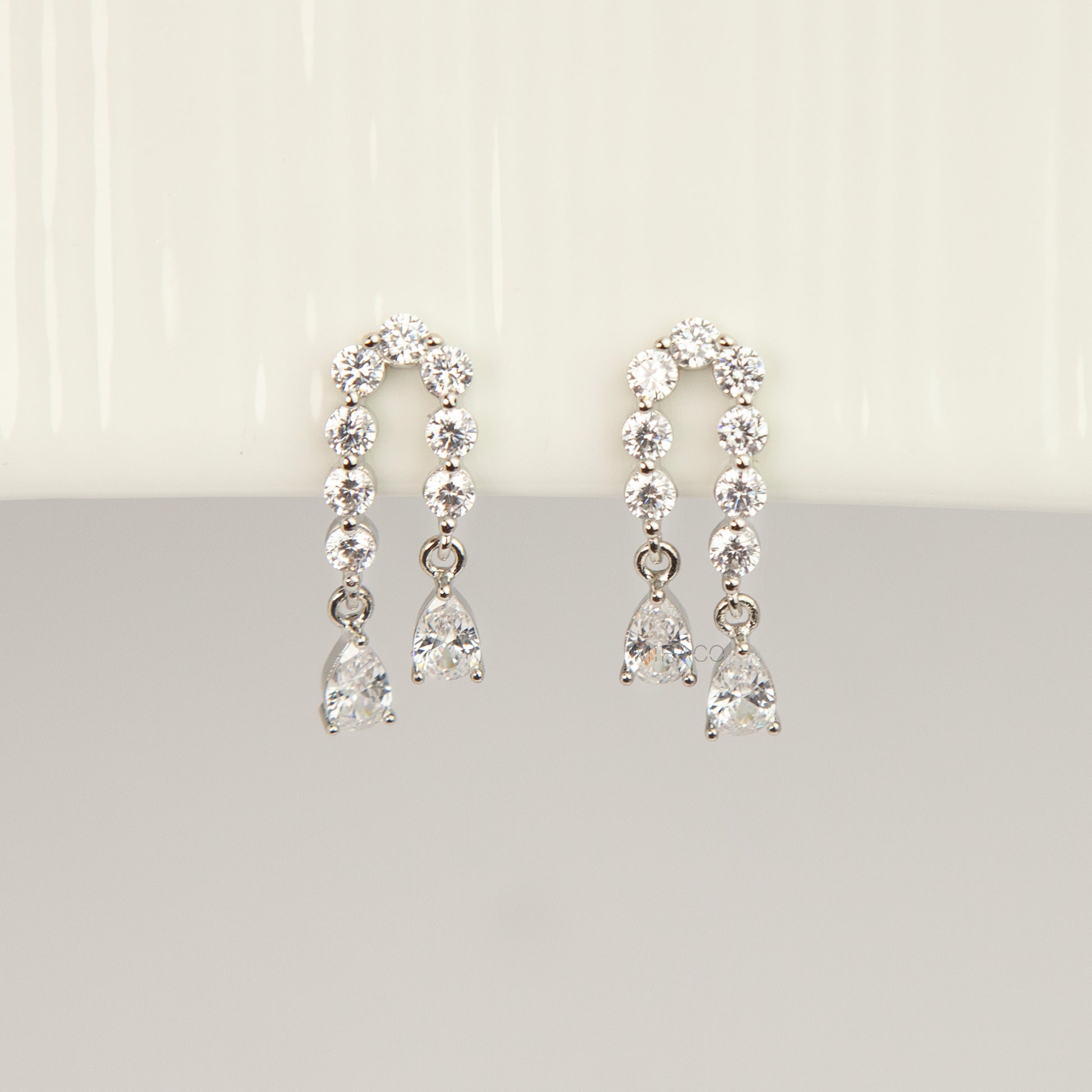 Silver non-pierced clip-on arch earrings with round silicone backs, paved with round cubic zirconia and finished with dangling teardrop crystal gems