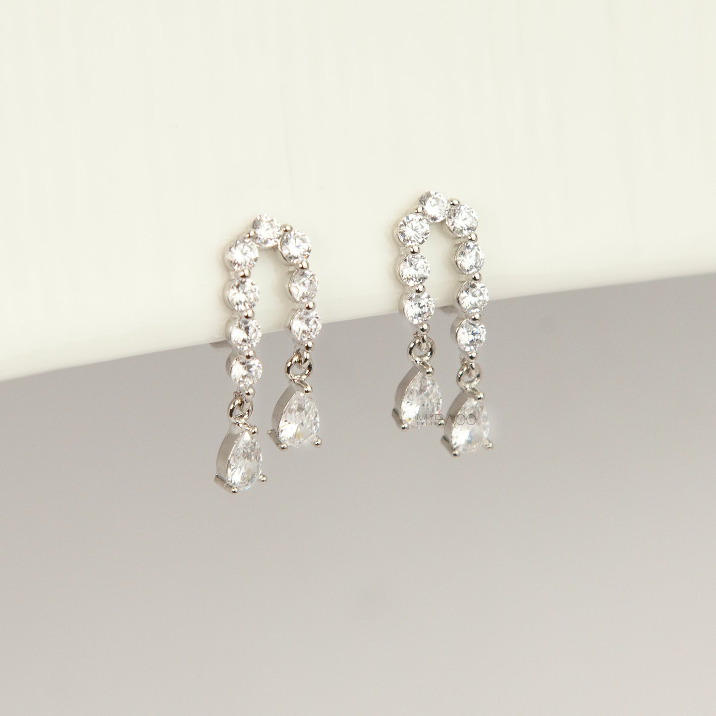 Silver non-pierced clip-on arch earrings with round silicone backs, paved with round cubic zirconia and finished with dangling teardrop crystal gems