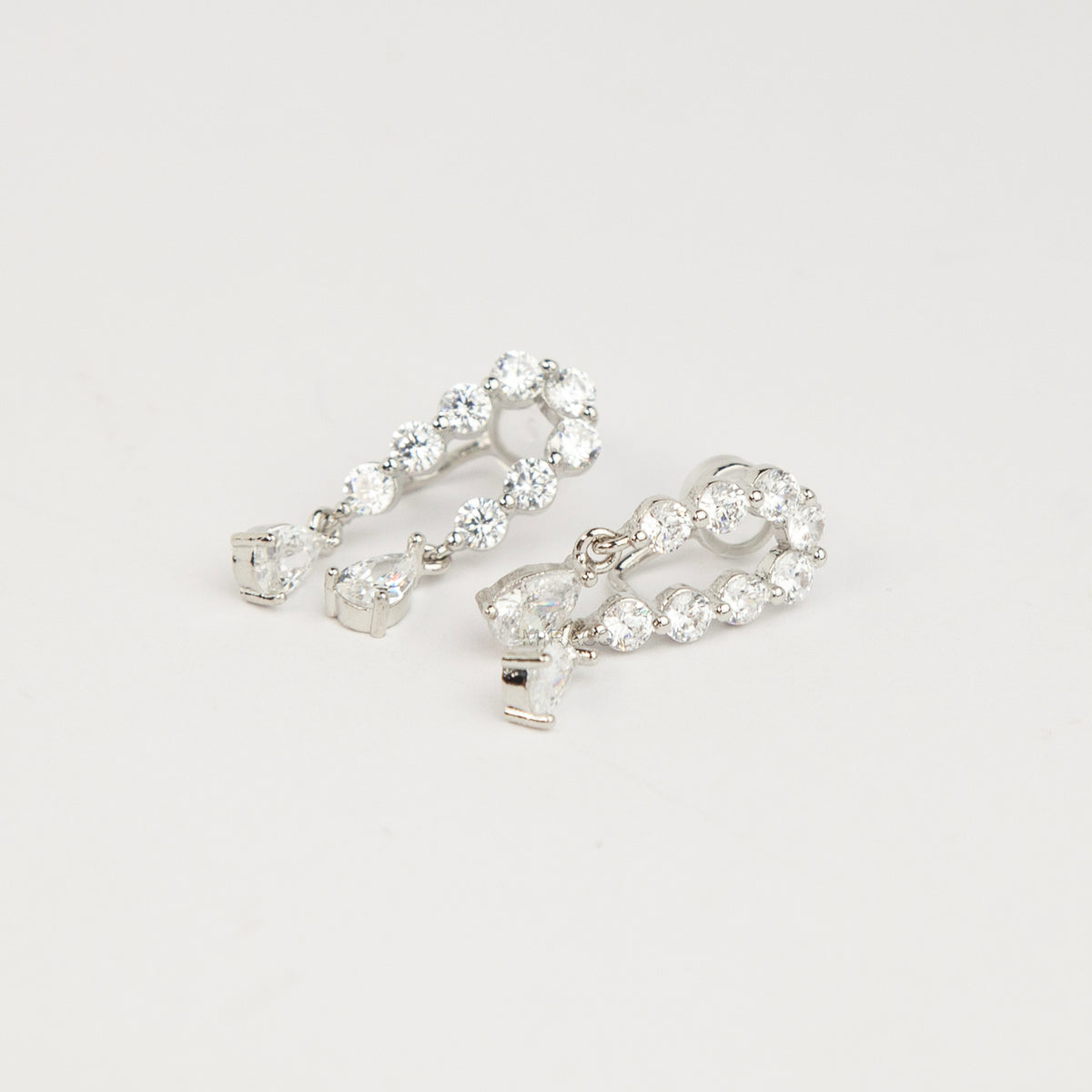 Silver non-pierced clip-on arch earrings with round silicone backs, paved with round cubic zirconia and finished with dangling teardrop crystal gems