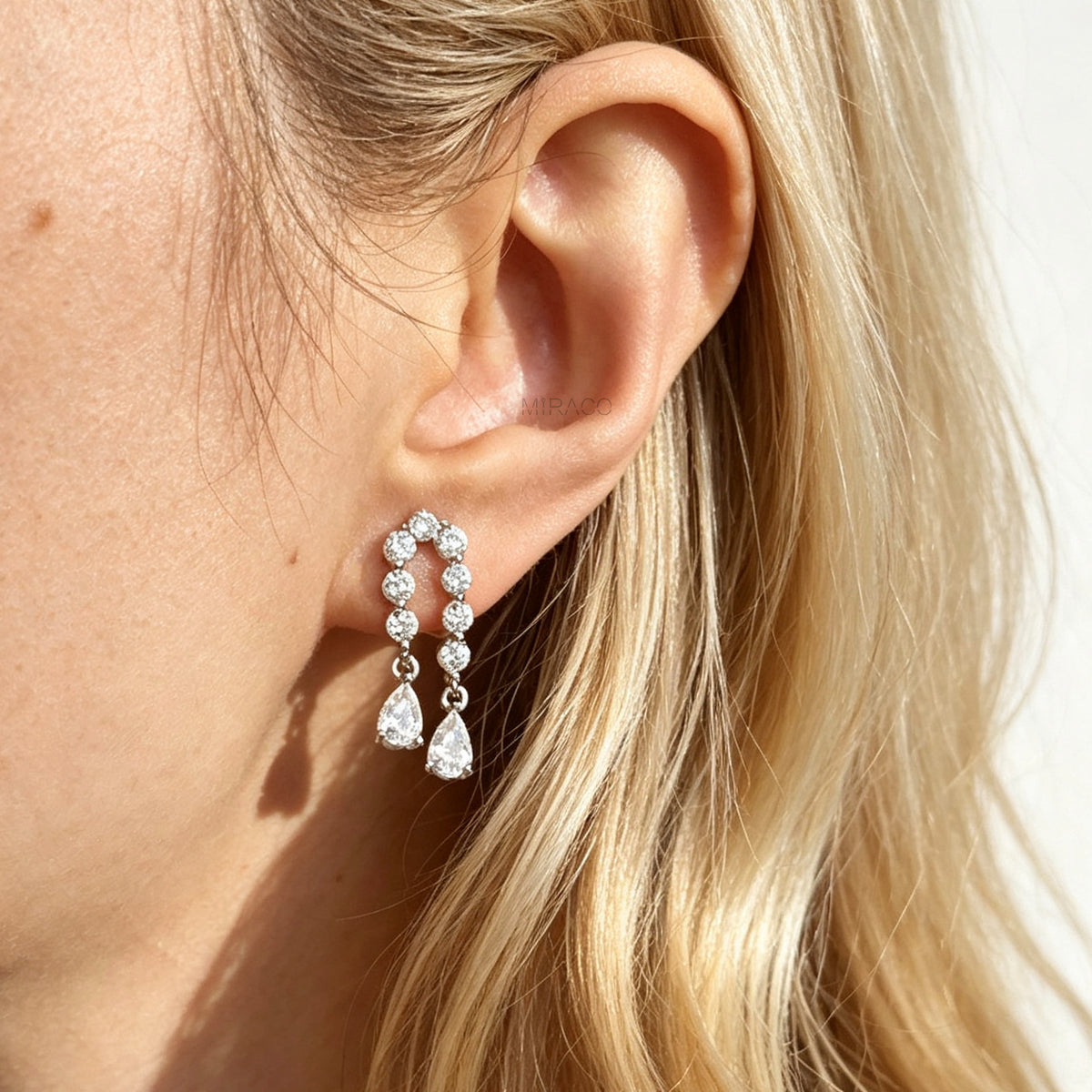 Silver non-pierced clip-on arch earrings with round silicone backs, paved with round cubic zirconia and finished with dangling teardrop crystal gems worn on a model.