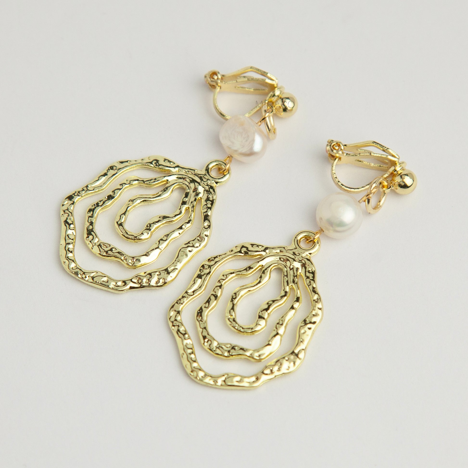 Gold mini-clip clip-on drop earrings featuring a natural freshwater pearl above a concentric hammered wavy openwork pendant