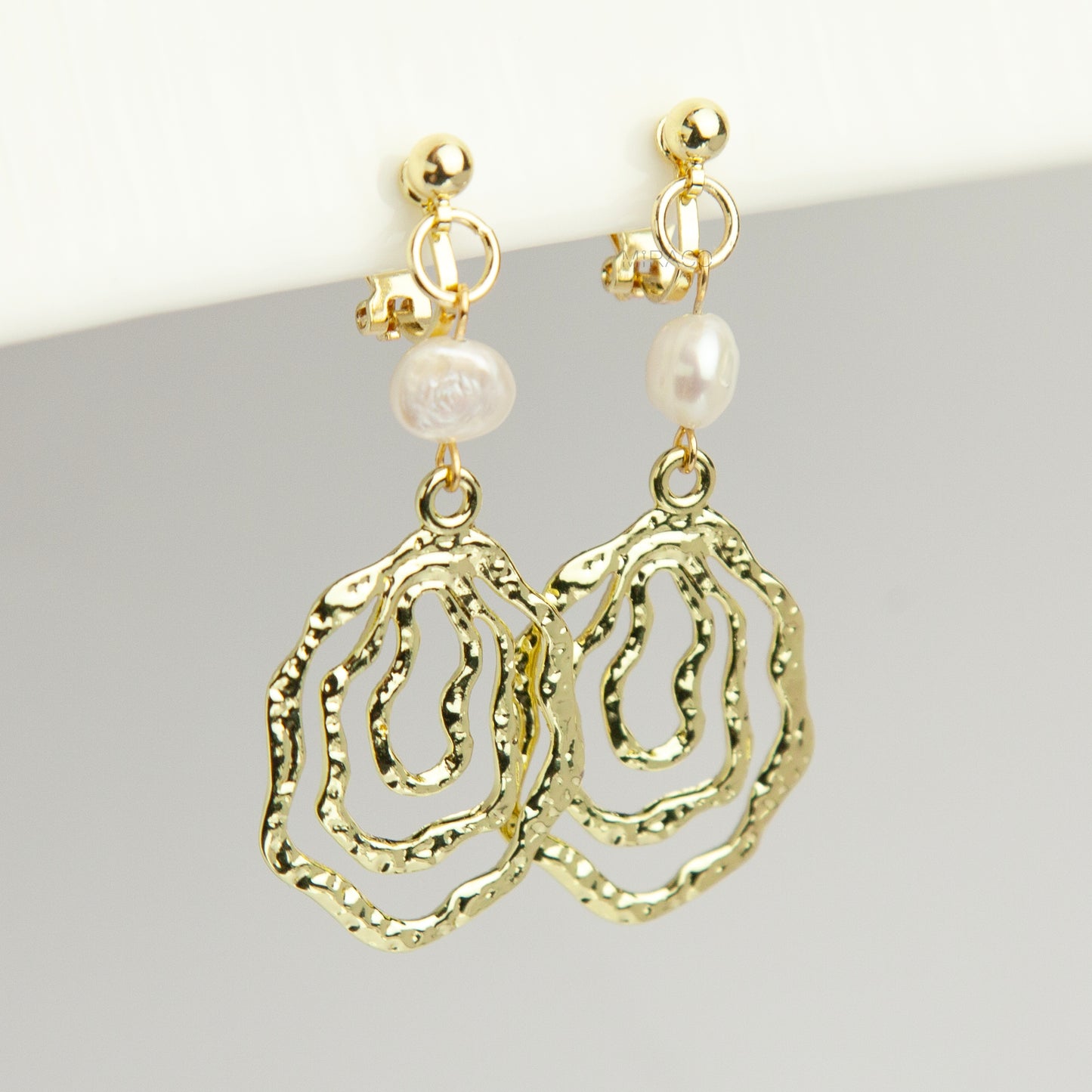 Gold mini-clip clip-on drop earrings featuring a natural freshwater pearl above a concentric hammered wavy openwork pendant