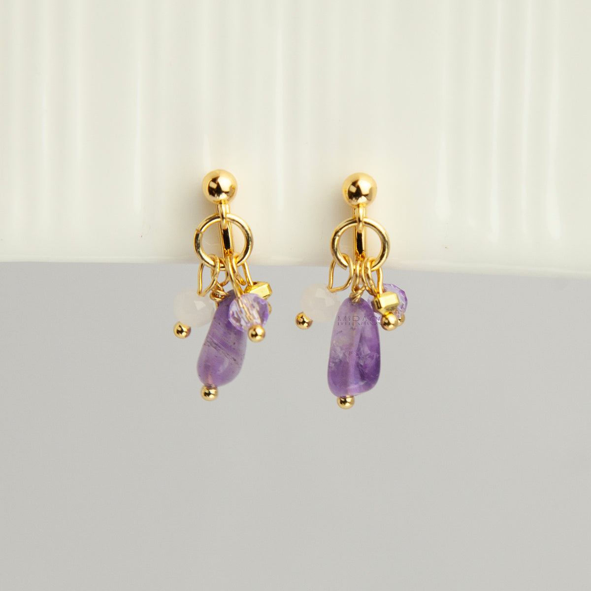 Gold screw-back clip-on hoop earrings with a raw purple amethyst stone, faceted lilac crystal charm, and white bead displayed on a light background.