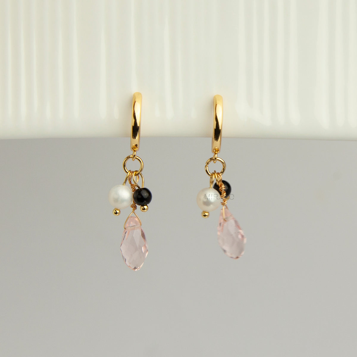 Gold screw-back clip-on hoop earrings featuring a faceted pink teardrop crystal charm, small white pearl, and black bead