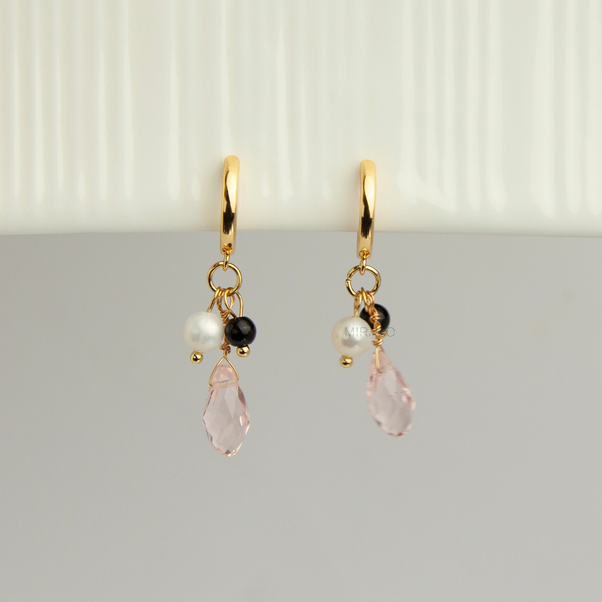 Gold screw-back clip-on hoop earrings featuring a faceted pink teardrop crystal charm, small white pearl, and black bead