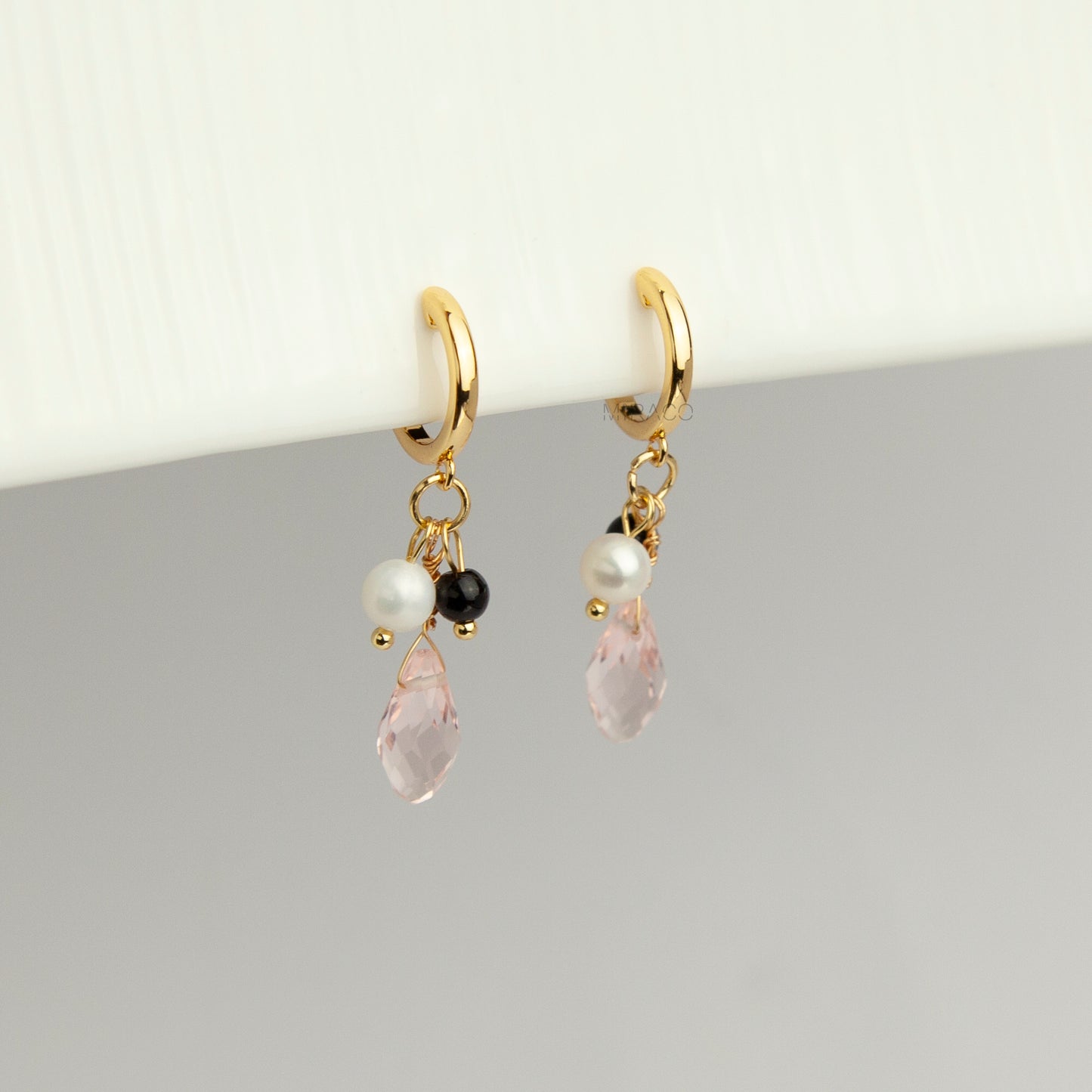 Gold screw-back clip-on hoop earrings featuring a faceted pink teardrop crystal charm, small white pearl, and black bead