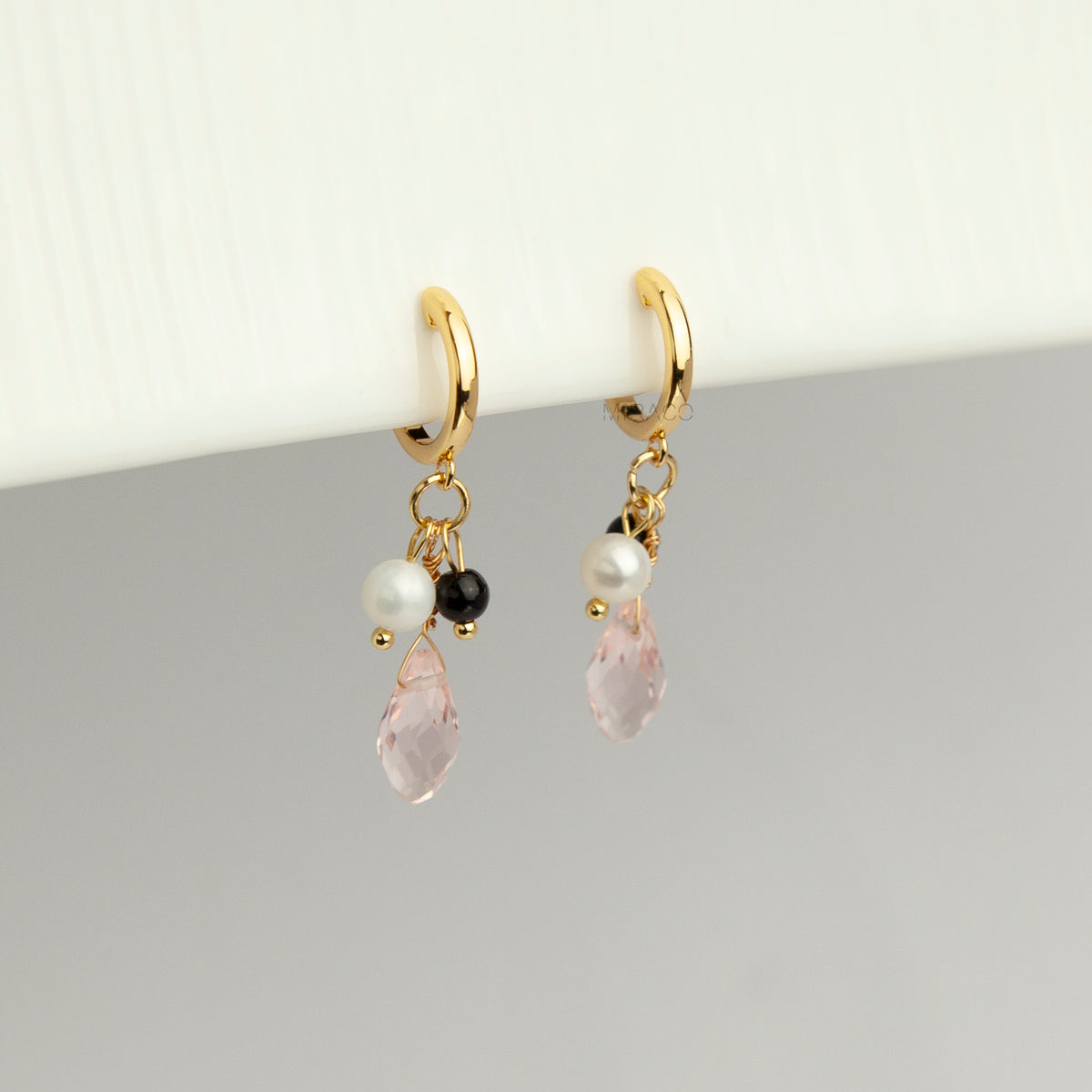 Gold screw-back clip-on hoop earrings featuring a faceted pink teardrop crystal charm, small white pearl, and black bead