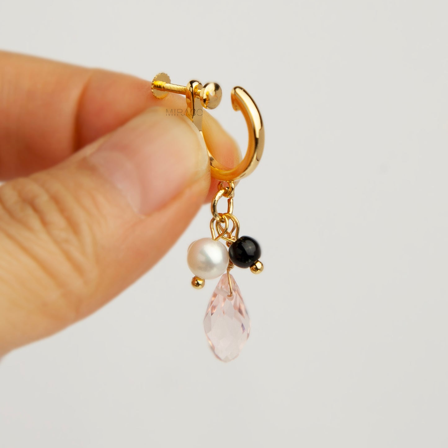 Gold screw-back clip-on hoop earrings featuring a faceted pink teardrop crystal charm, small white pearl, and black bead