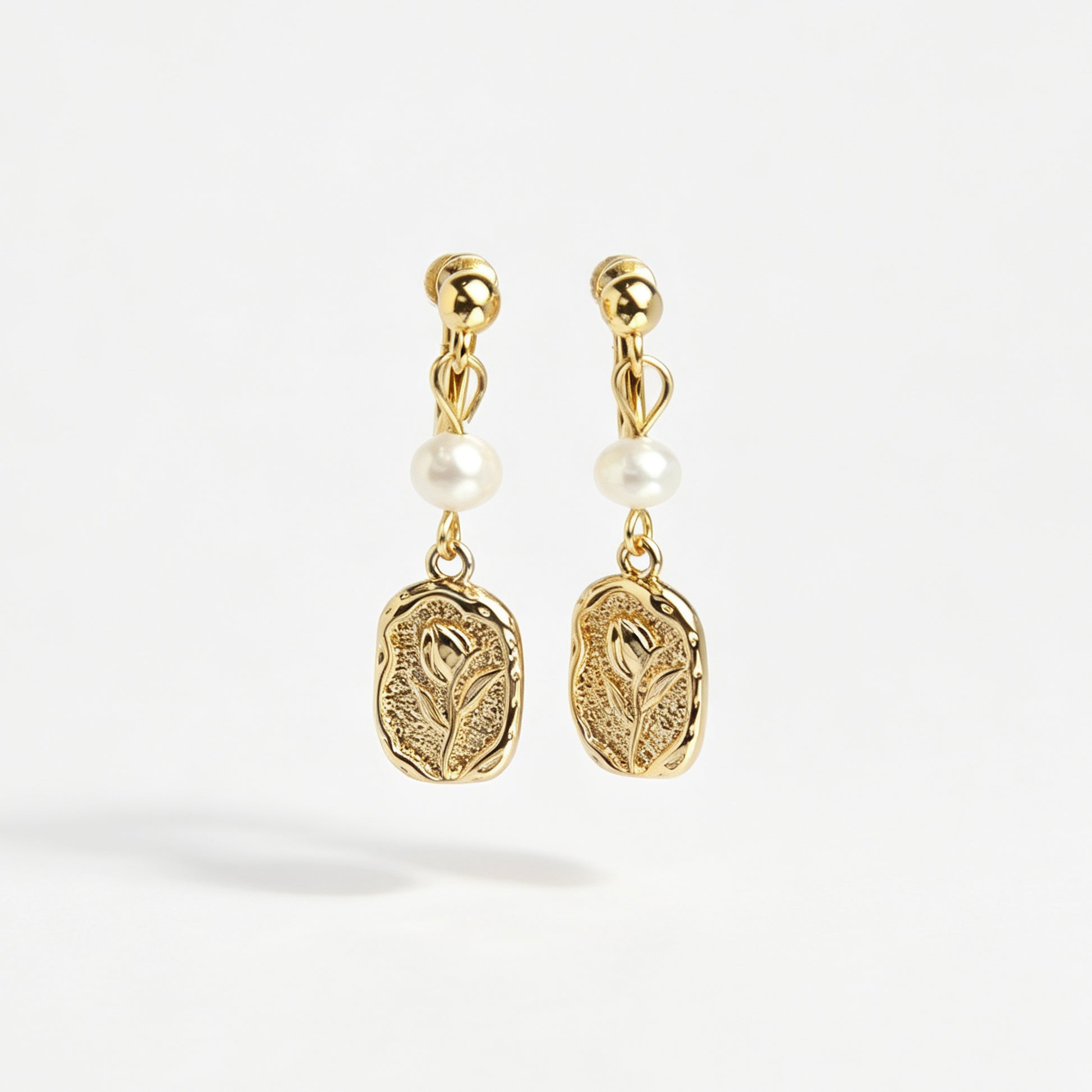 Gold screw-back clip-on drop earrings featuring a lustrous white pearl and a textured oval medallion with an embossed floral design