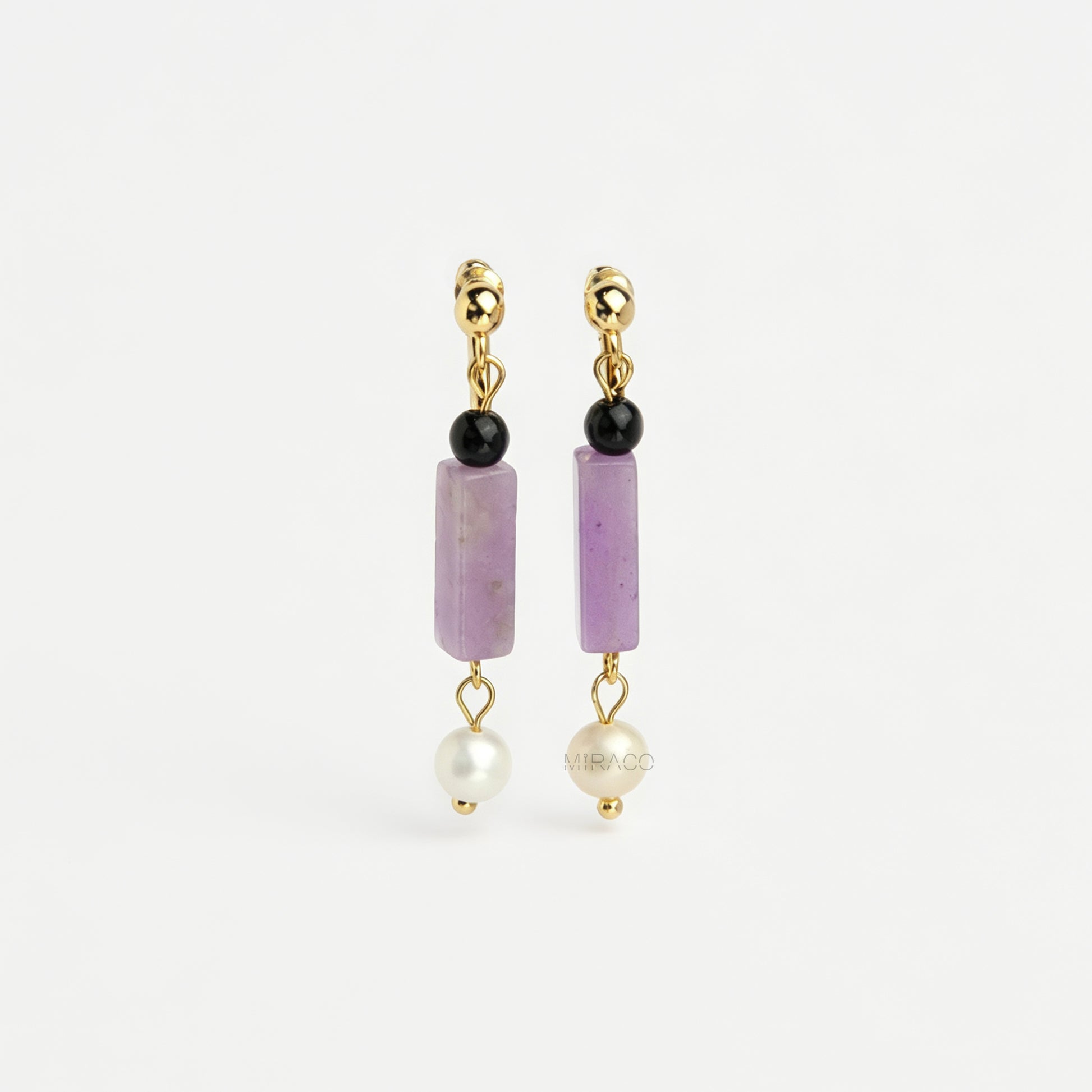 Gold screw-back clip-on drop earrings featuring a black onyx bead, rectangular purple jade stone, and dangling white freshwater pearl.