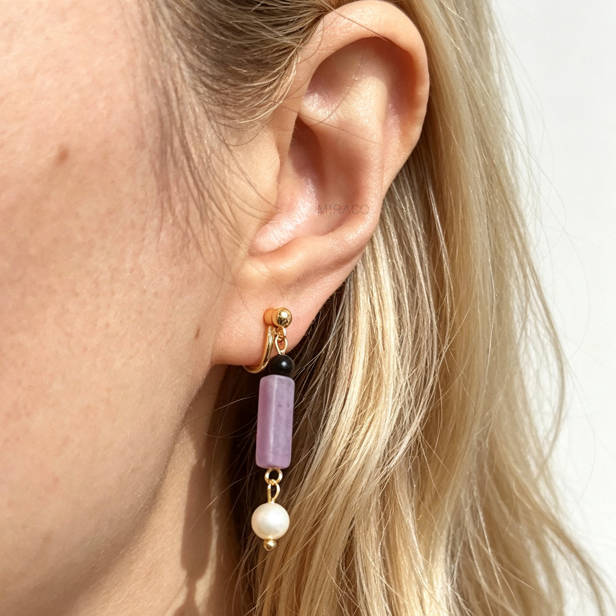 Gold screw-back clip-on drop earrings featuring a black onyx bead, rectangular purple jade stone, and dangling white freshwater pearl.