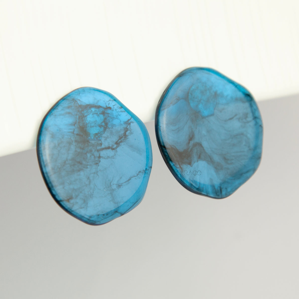 Large organic oval clip-on earring featuring a blue and black marbled resin design