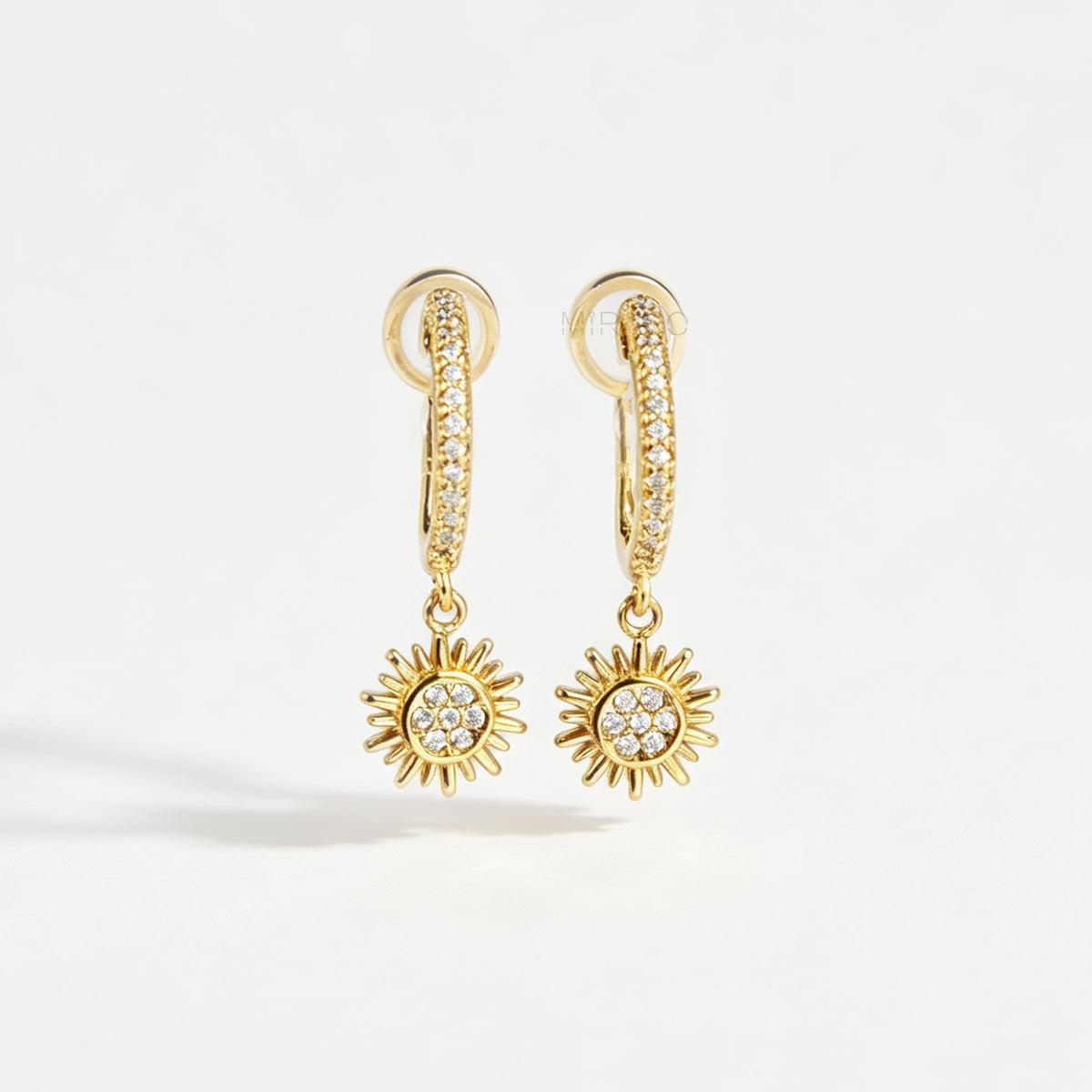 Gold clip-on hoop earrings with pave cubic zirconia pavé detailing, dangling celestial sunburst charms, and clear round silicone comfort backings.