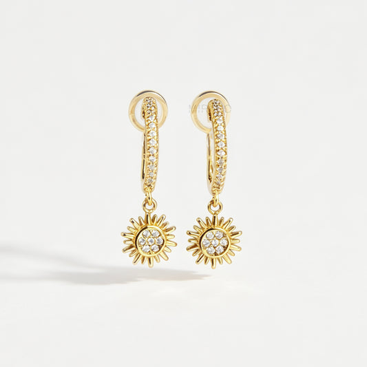 Gold clip-on hoop earrings with pave cubic zirconia pavé detailing, dangling celestial sunburst charms, and clear round silicone comfort backings.