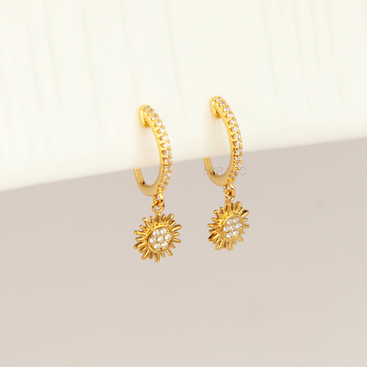 Gold clip-on hoop earrings with pave cubic zirconia pavé detailing, dangling celestial sunburst charms, and clear round silicone comfort backings.