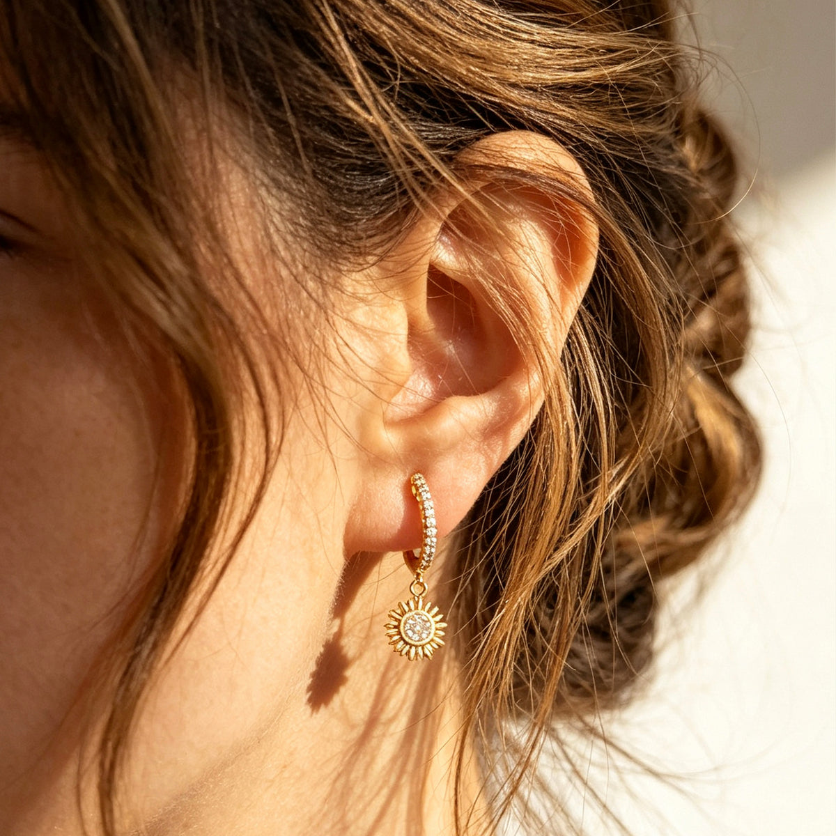 Gold clip-on hoop earrings with pave cubic zirconia pavé detailing, dangling celestial sunburst charms, and clear round silicone comfort backings.